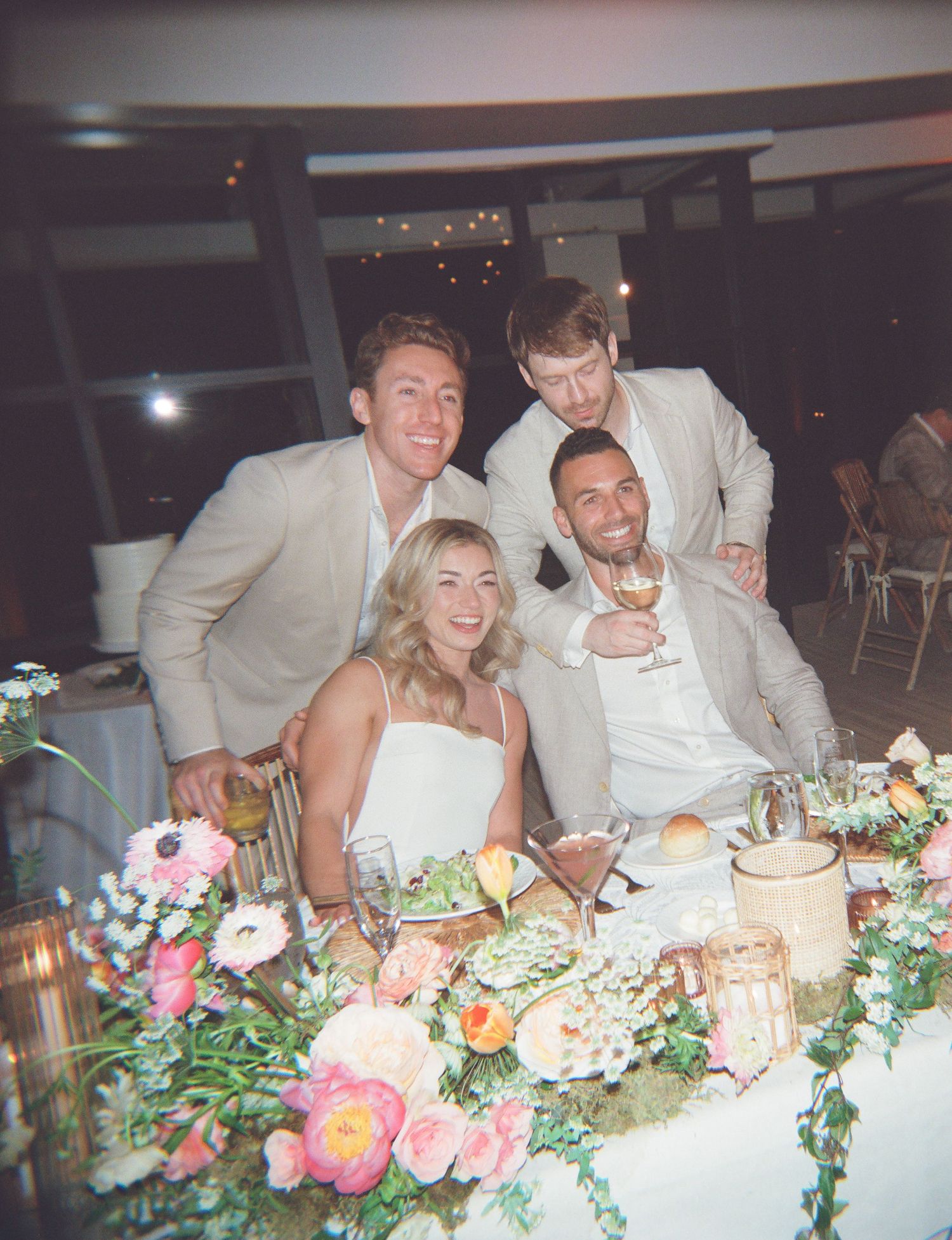 Wedding reception table scene with guests enjoying dinner among floral centerpieces.