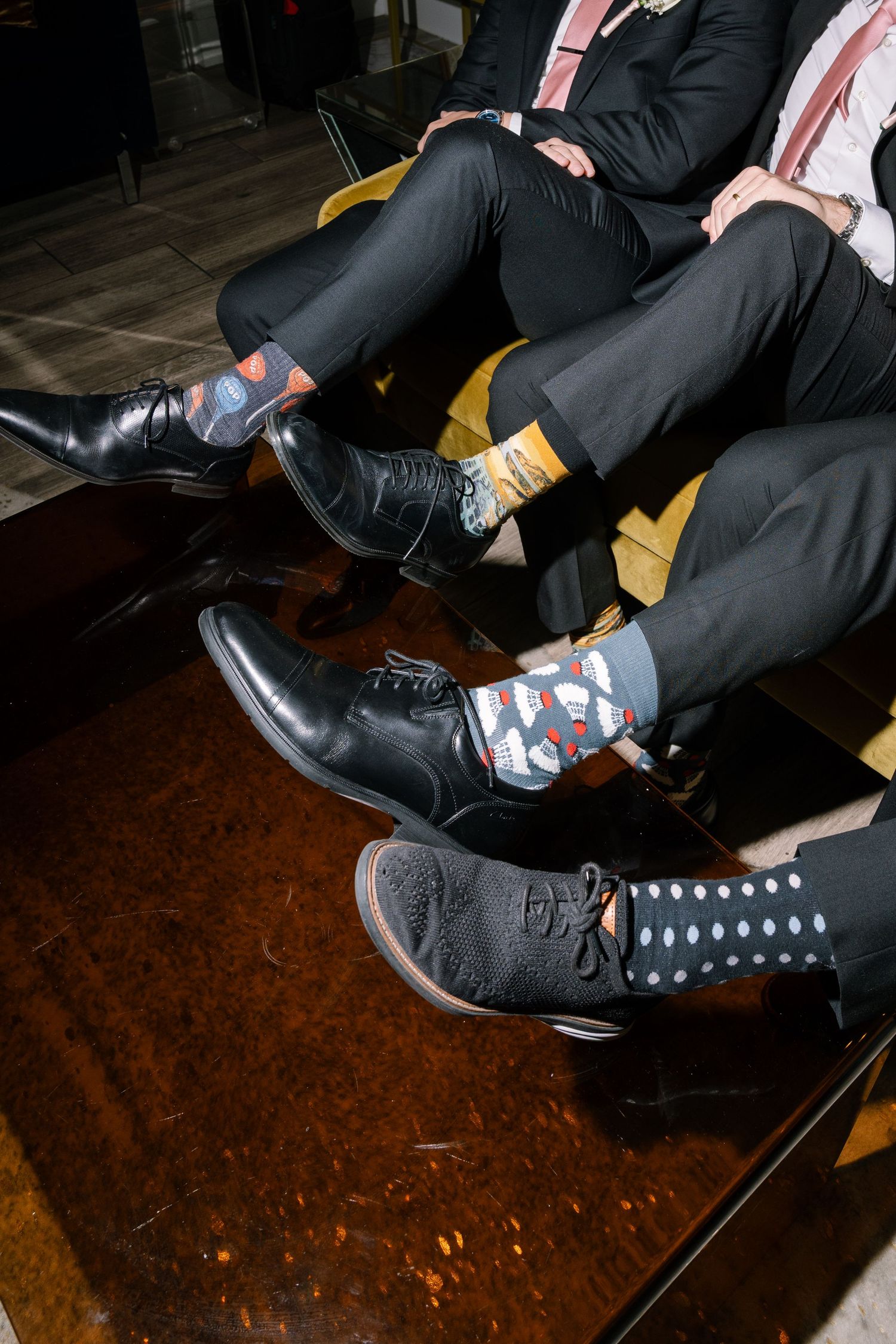 Groomsmen showing off colorful patterned wedding socks with black dress shoes and suits at wedding reception.