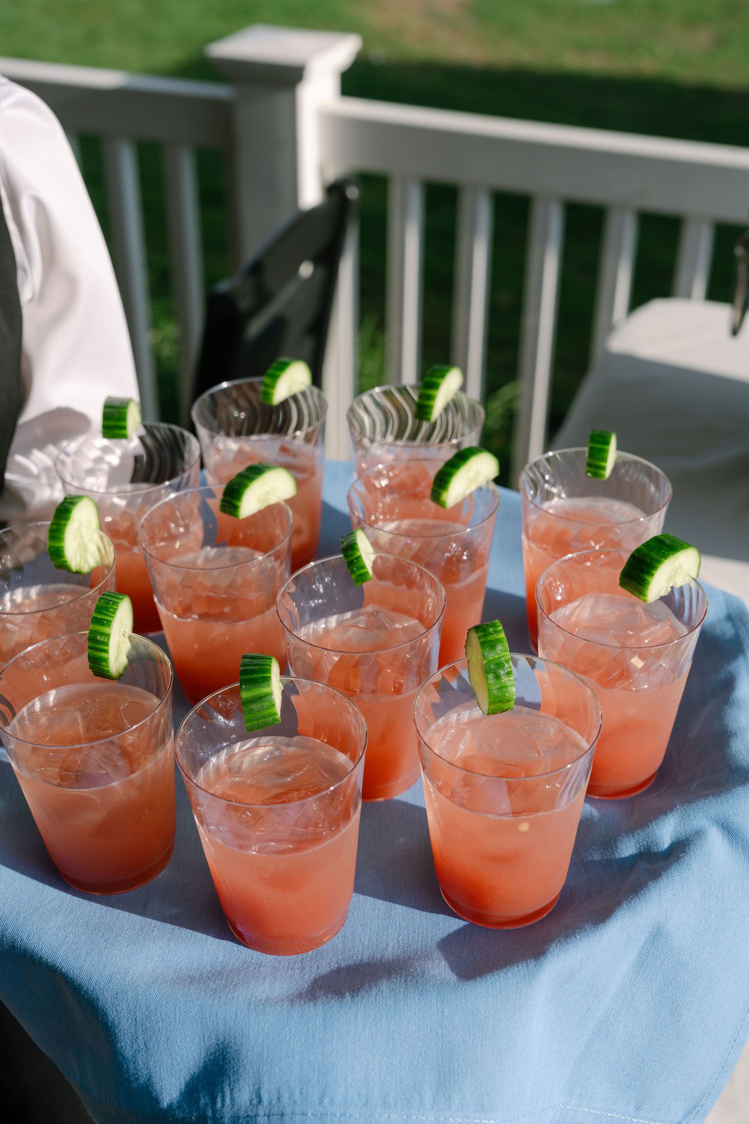 Tray of pink watermelon cocktails garnished with cucumber slices served at outdoor wedding reception.