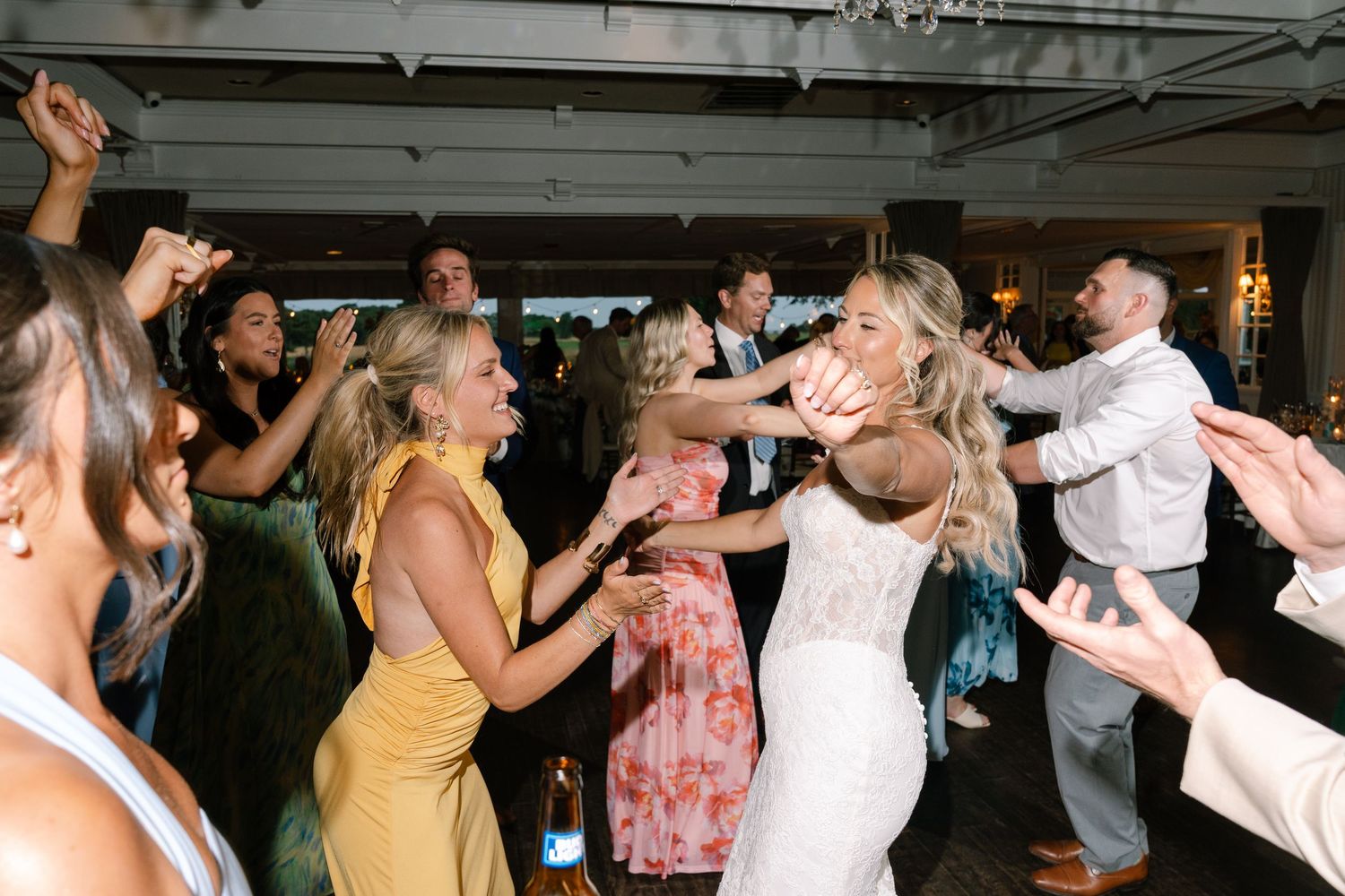 Bride in white lace gown dancing energetically with guests at lively wedding reception party.