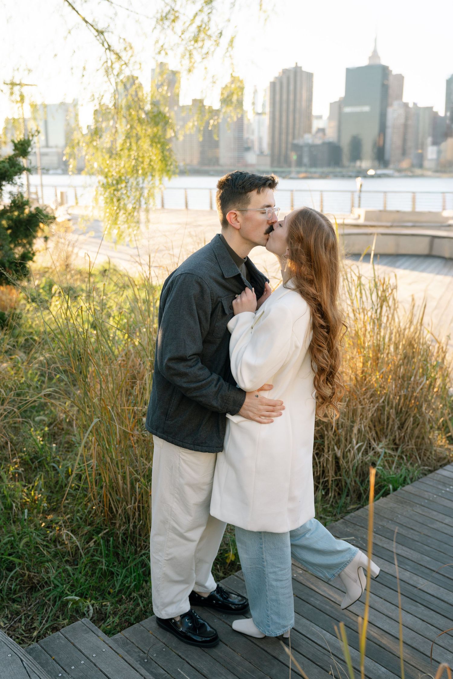 Romantic moment shared on boardwalk with NYC skyline and autumn grasses in background.