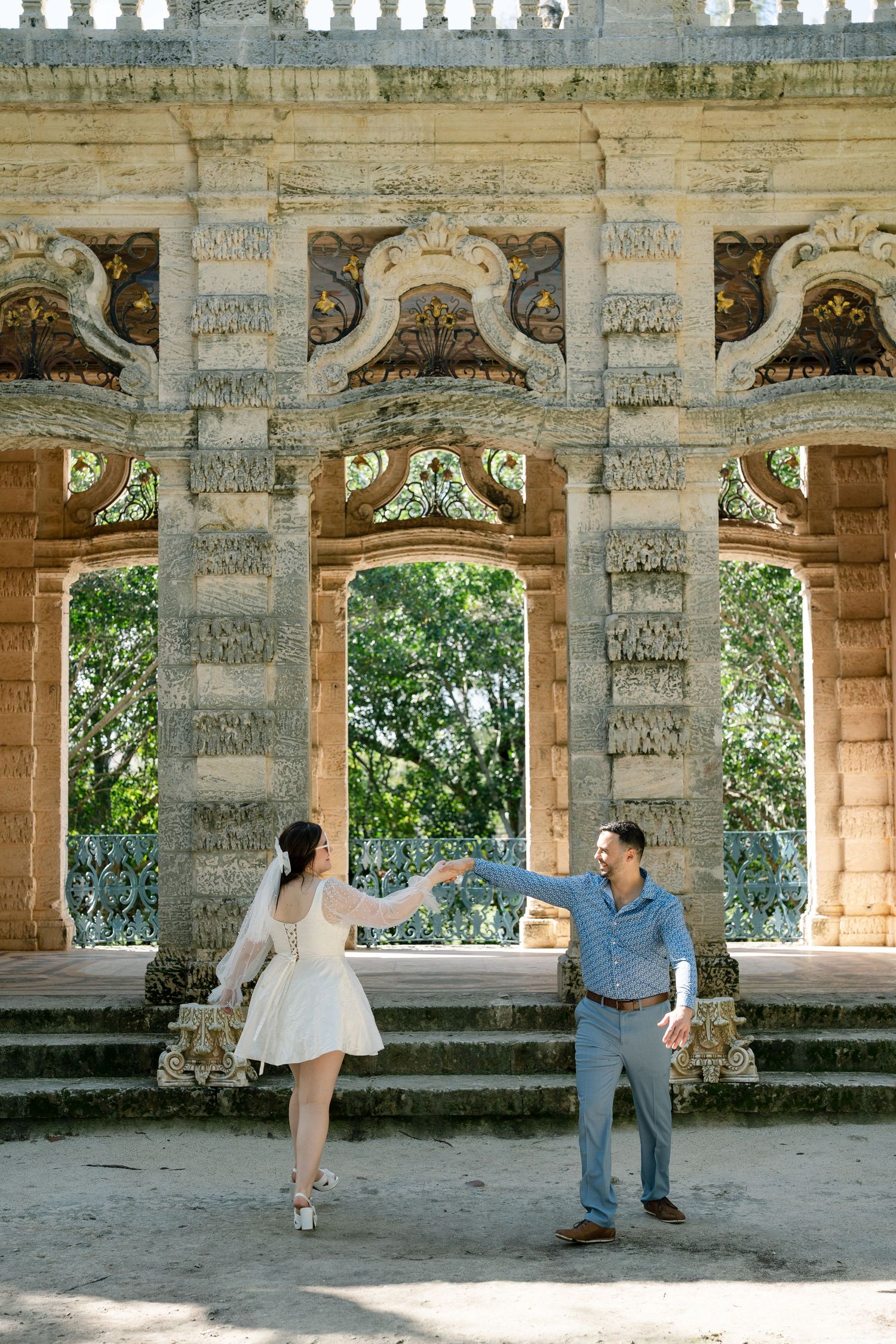 Classical stone colonnade with ornate carvings and repeating arches in a historic garden setting.