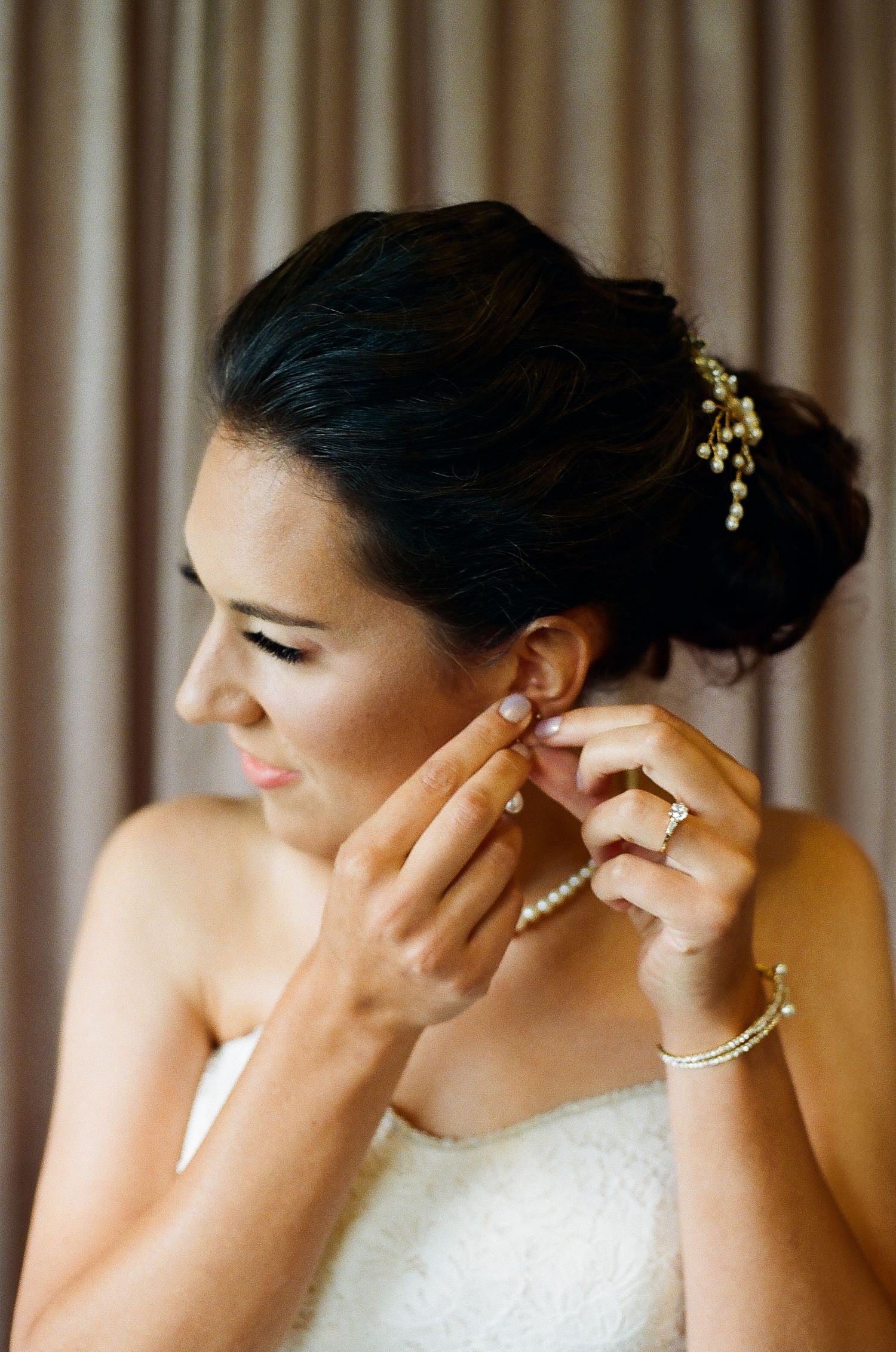 A bride getting ready for her wedding while putting on elegant gold earrings and jewelry.