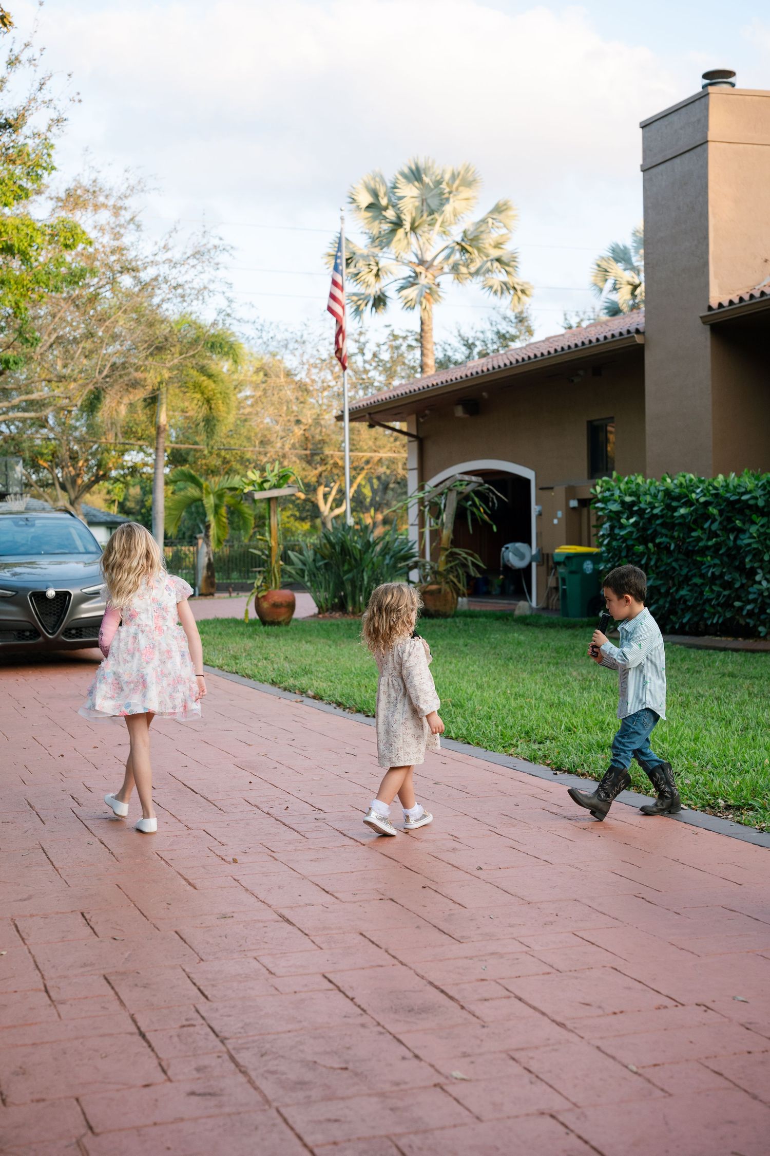 Children walking on terracotta tiles outside a Spanish-style building with an American flag.
