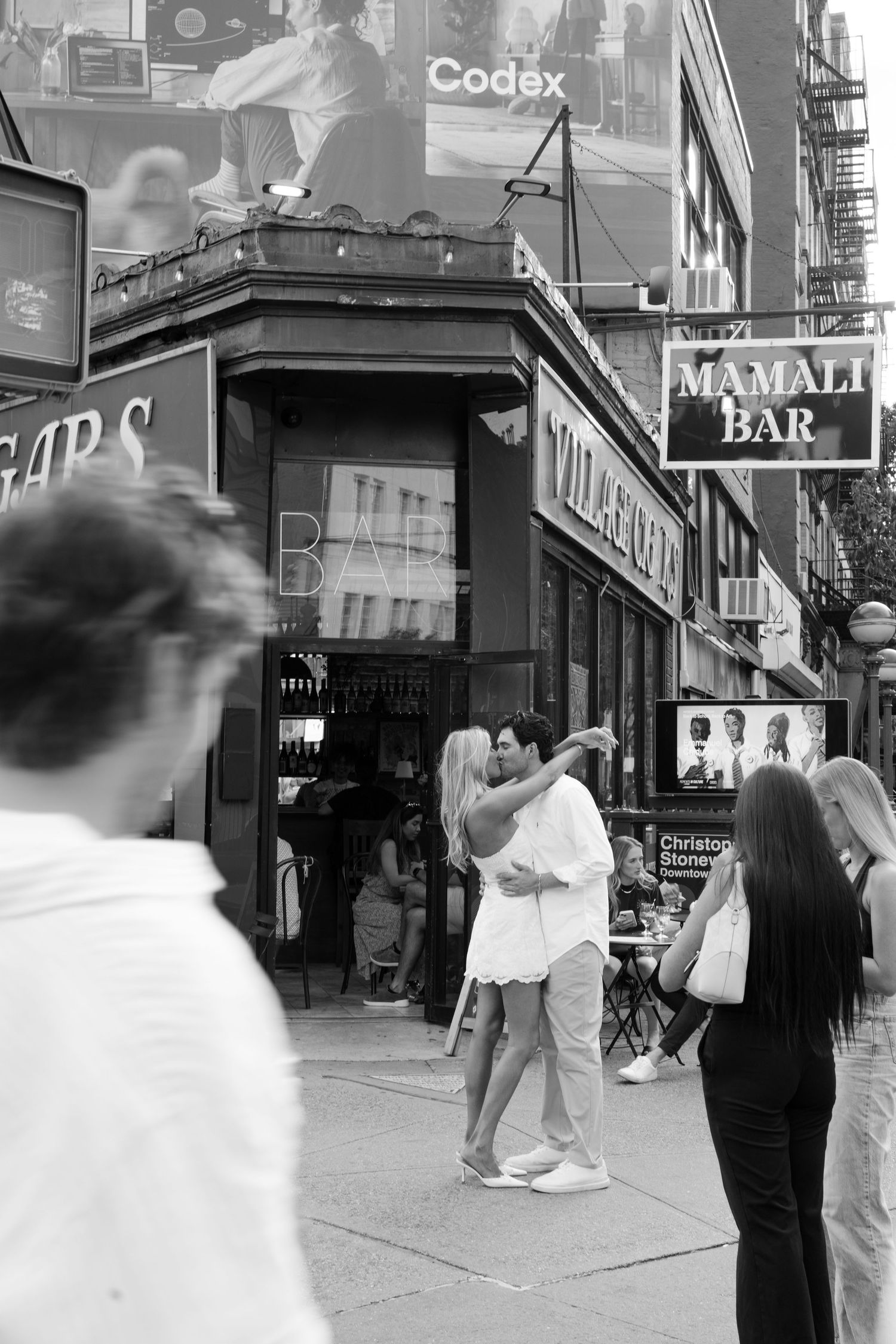 Black and white street photo of a couple embracing on a busy NYC sidewalk near Mamali Bar.