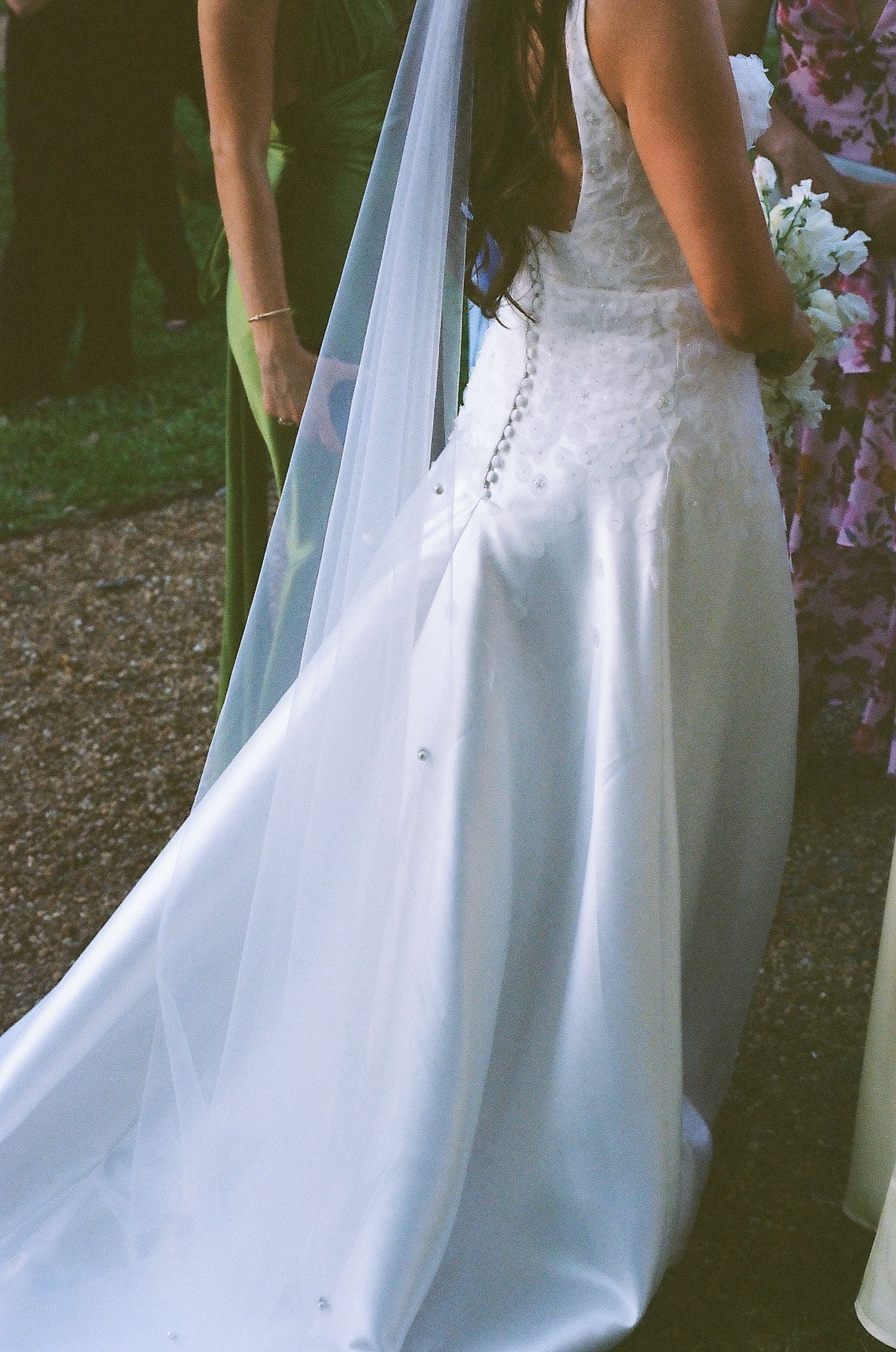 Close-up of bride in white satin wedding gown with long veil and lace bodice detail.