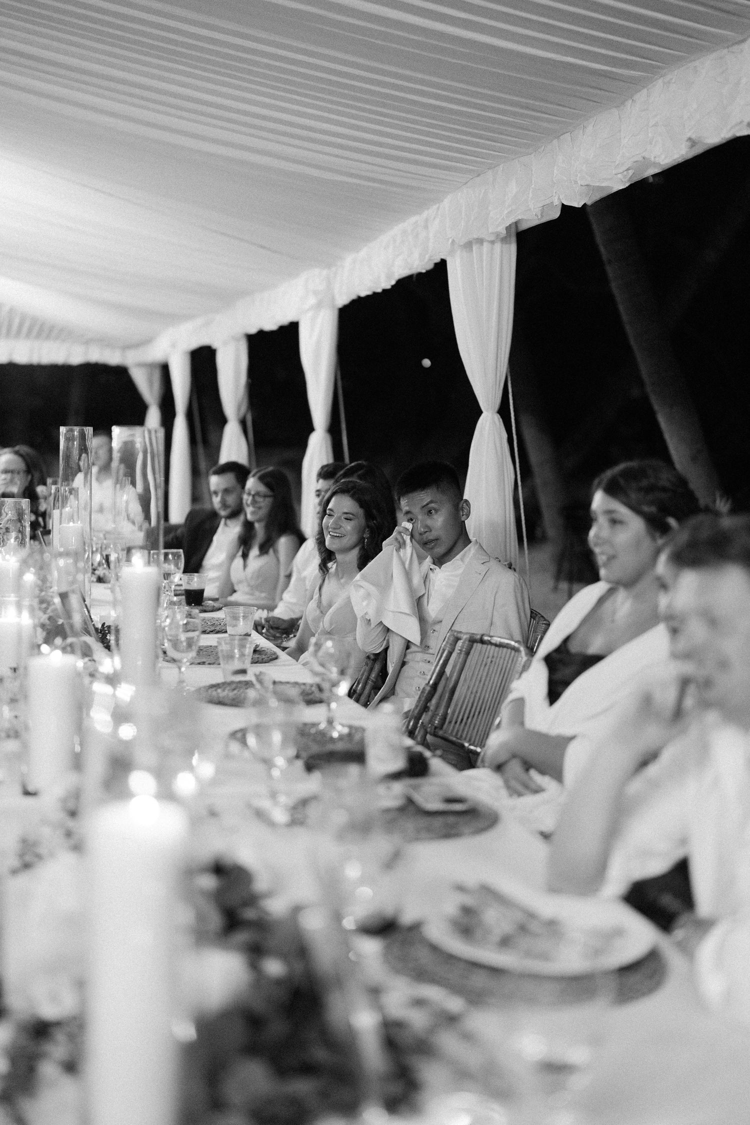 Wedding guests dining under a white tent canopy at long tables set for an elegant reception.