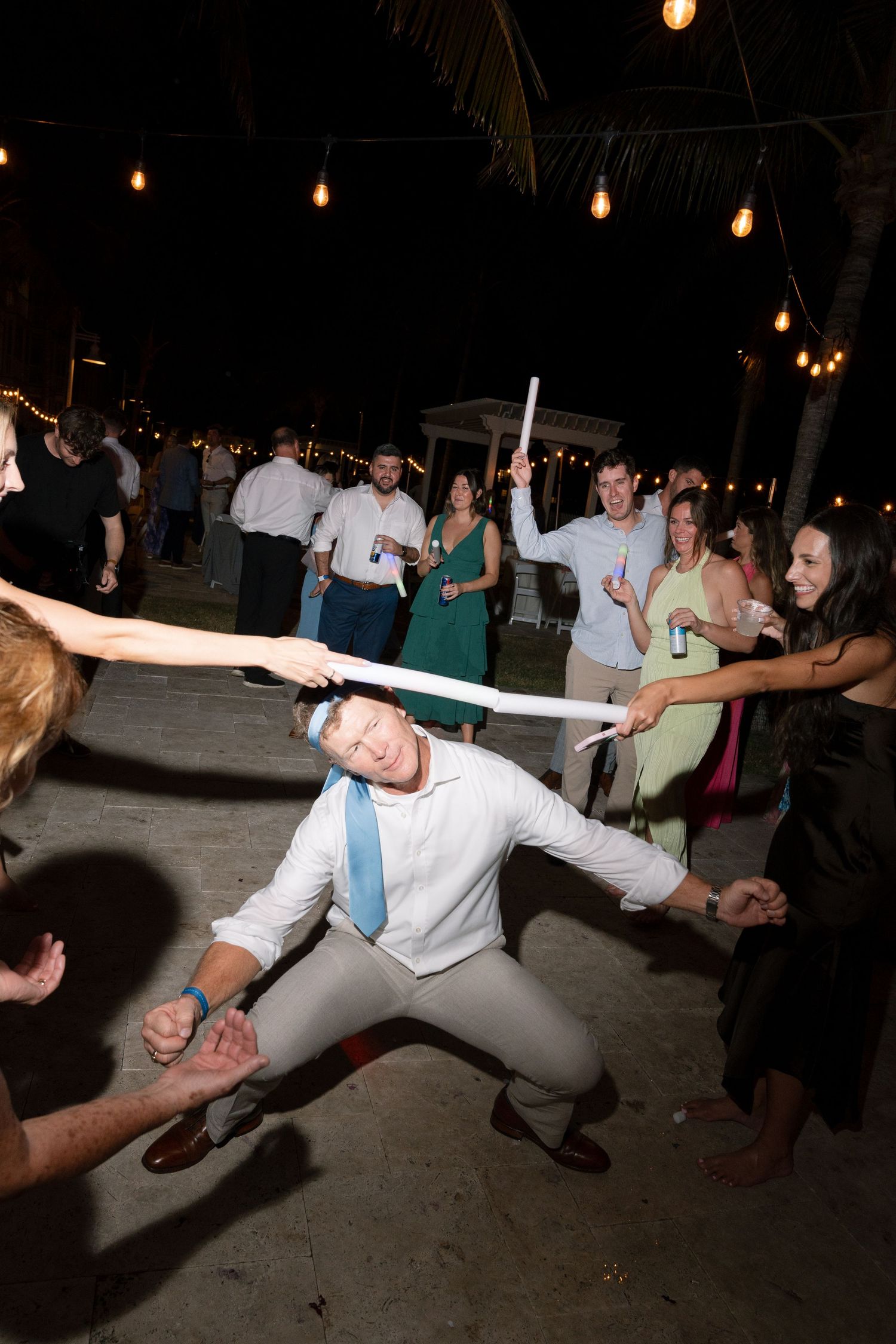 Wedding party guests dancing and doing limbo under a string of lights at an evening reception celebration.