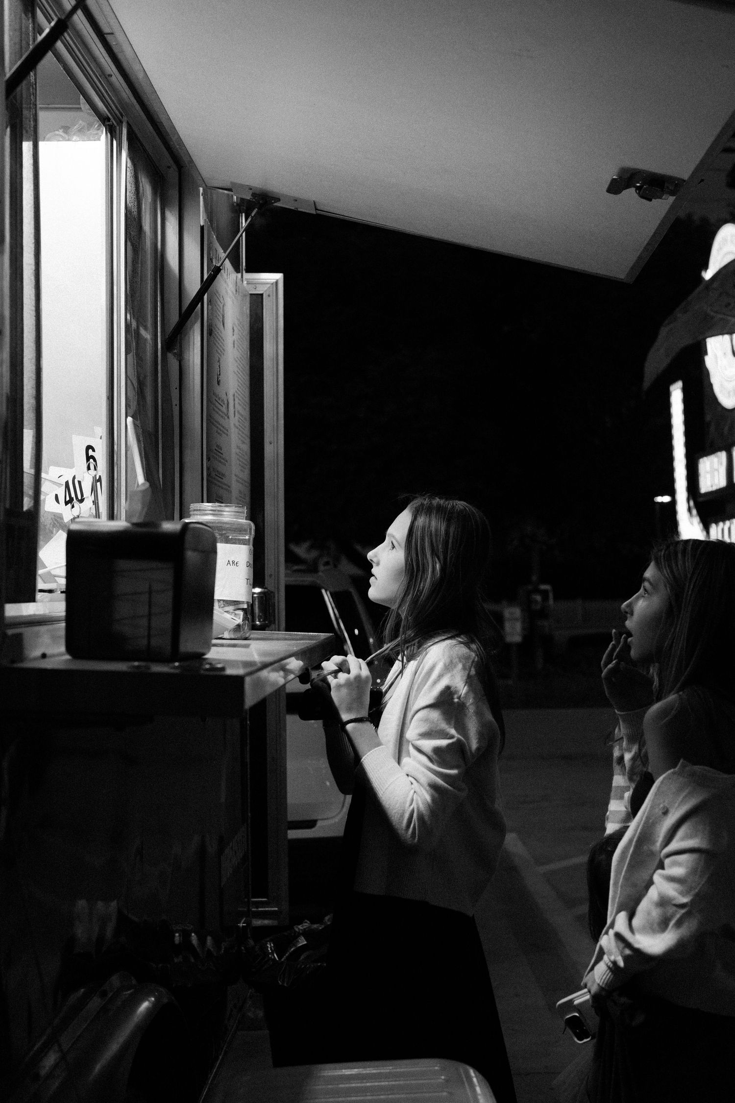 Black and white photo of people looking through windows in a dimly lit interior space.