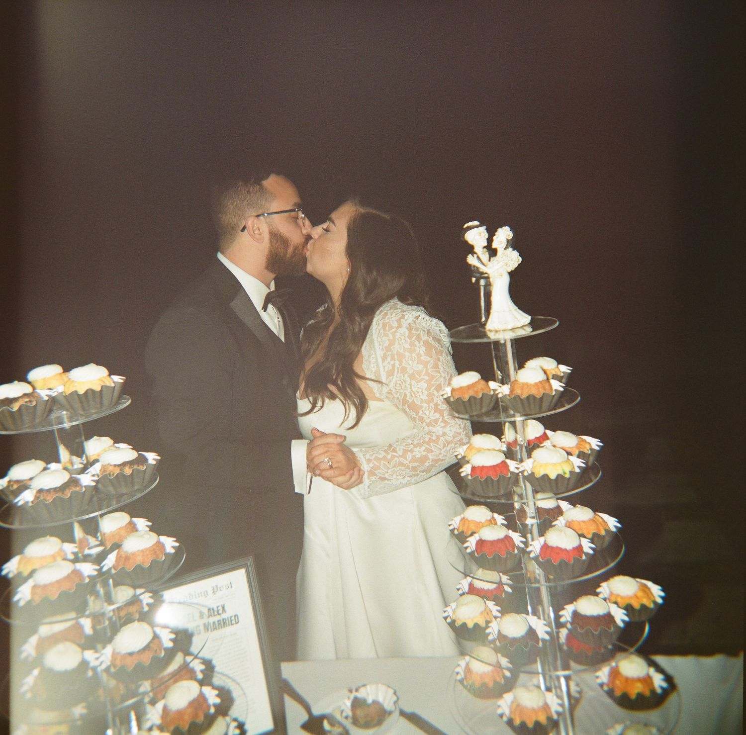 A couple sharing a kiss at their wedding reception with tiered cupcake displays decorated with umbrellas in the foreground.