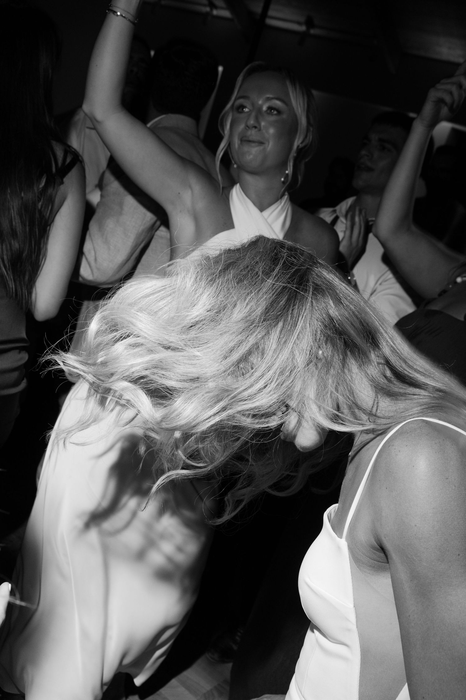 Black and white candid photo of wedding guests dancing energetically with hair in motion at a reception.