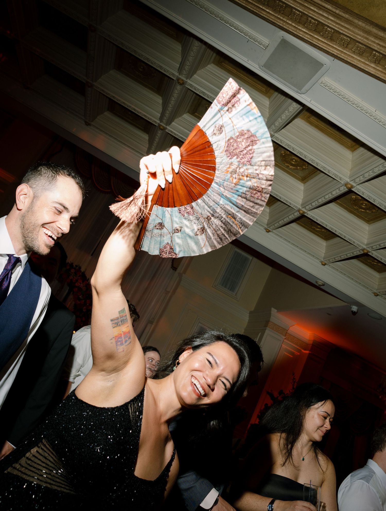 Guests dancing and celebrating with decorative fans at an indoor wedding reception.