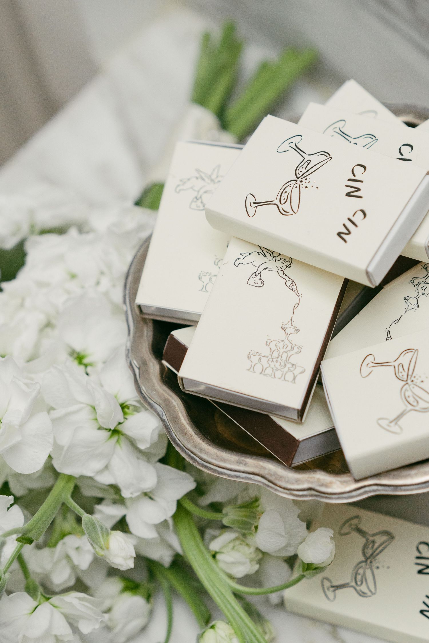 White wedding favor boxes with minimalist line drawings arranged among white floral decorations.