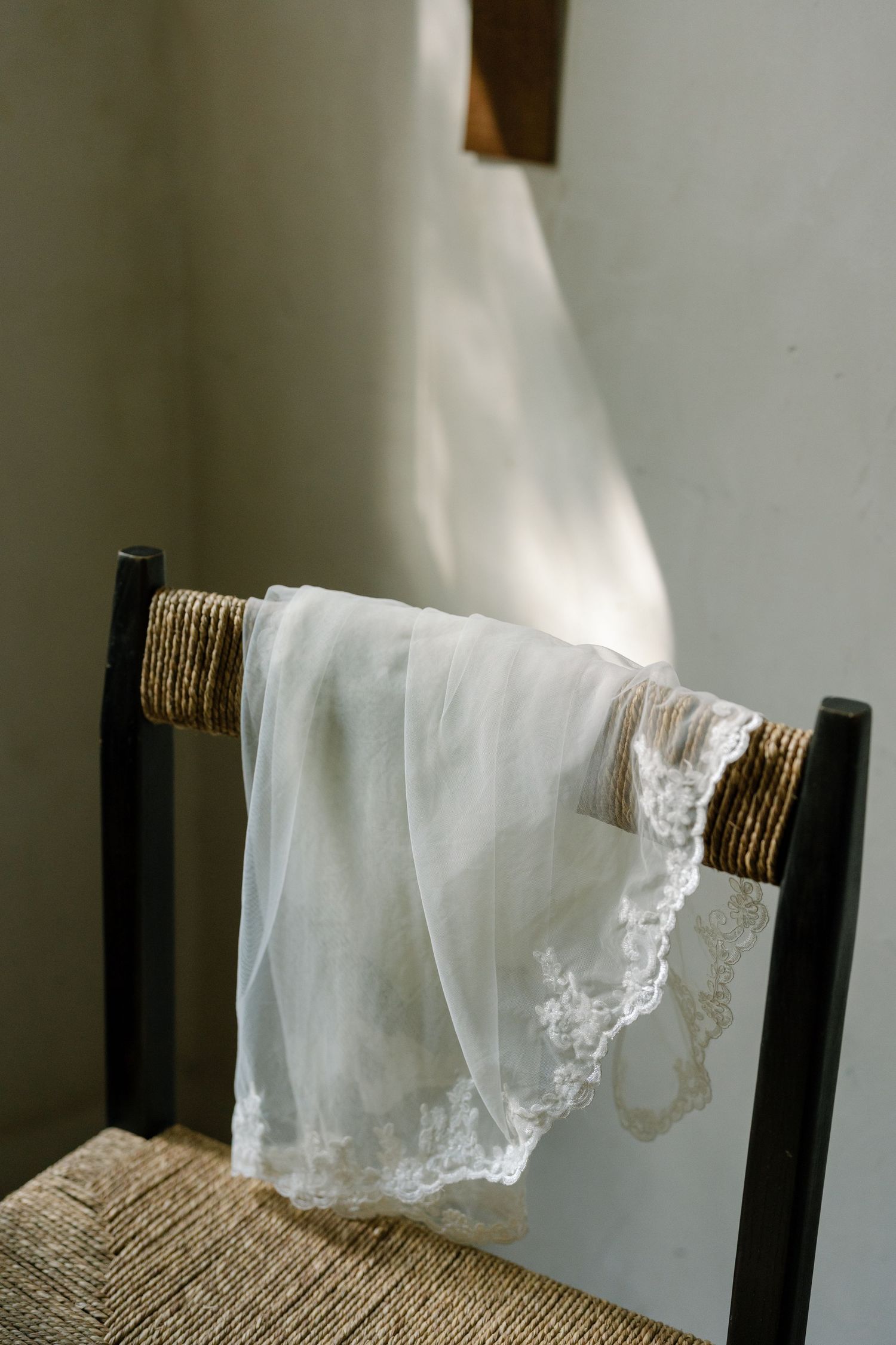 Delicate white lace handkerchief draped over a wooden chair in soft natural light.