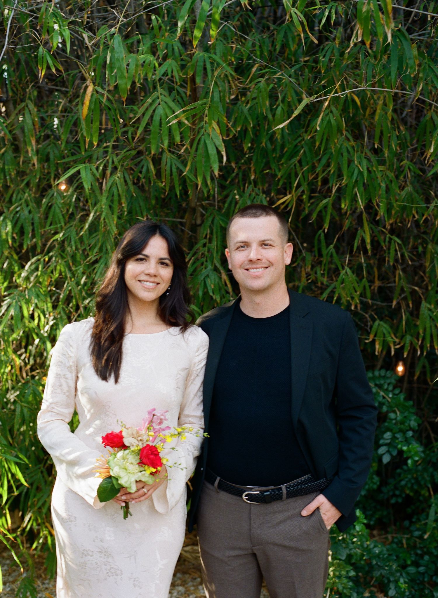 Outdoor portrait series with bamboo grove backdrop and red floral bouquet.