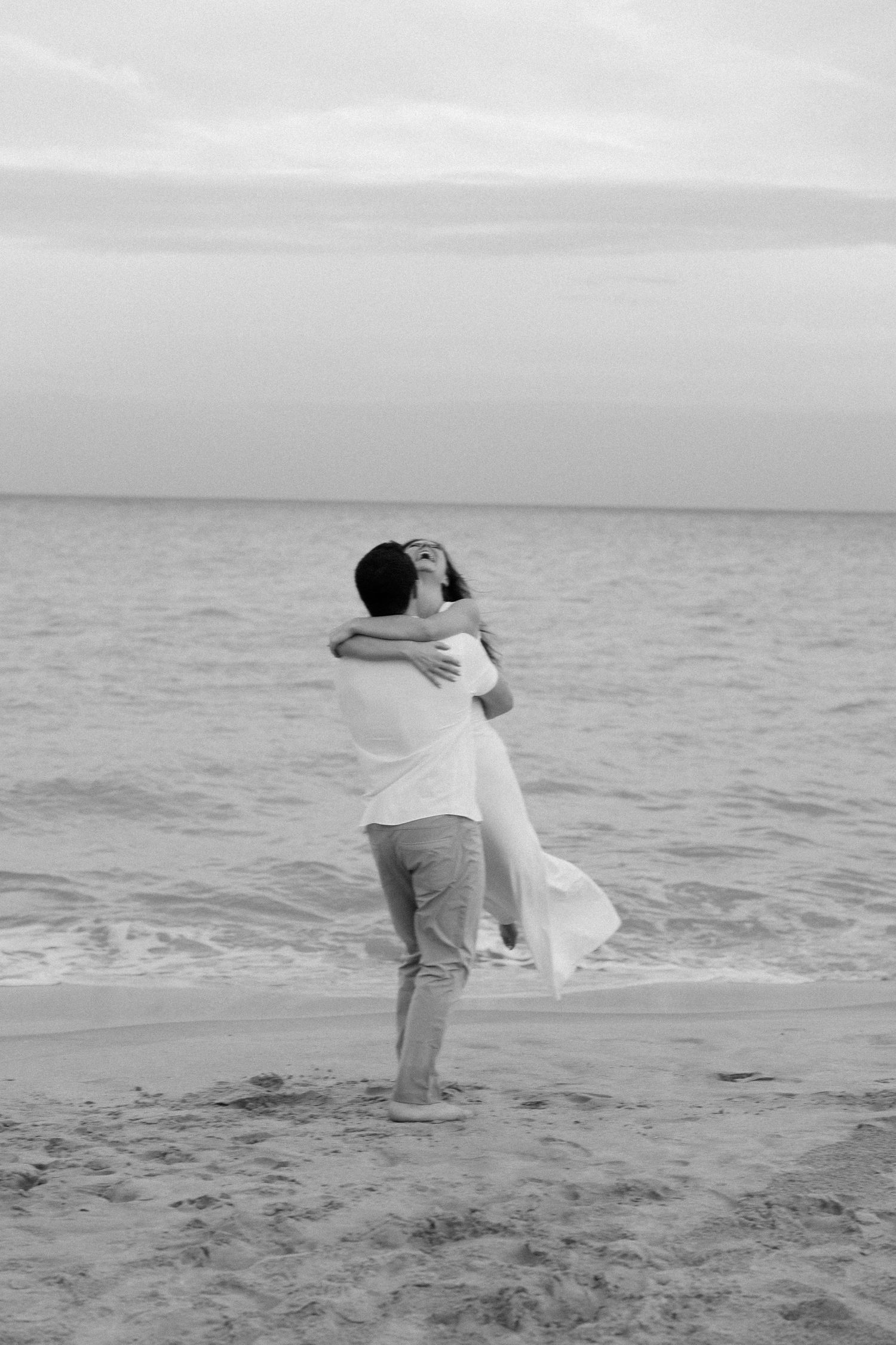 A black and white photo captures a couple's romantic moment standing in the ocean waves.