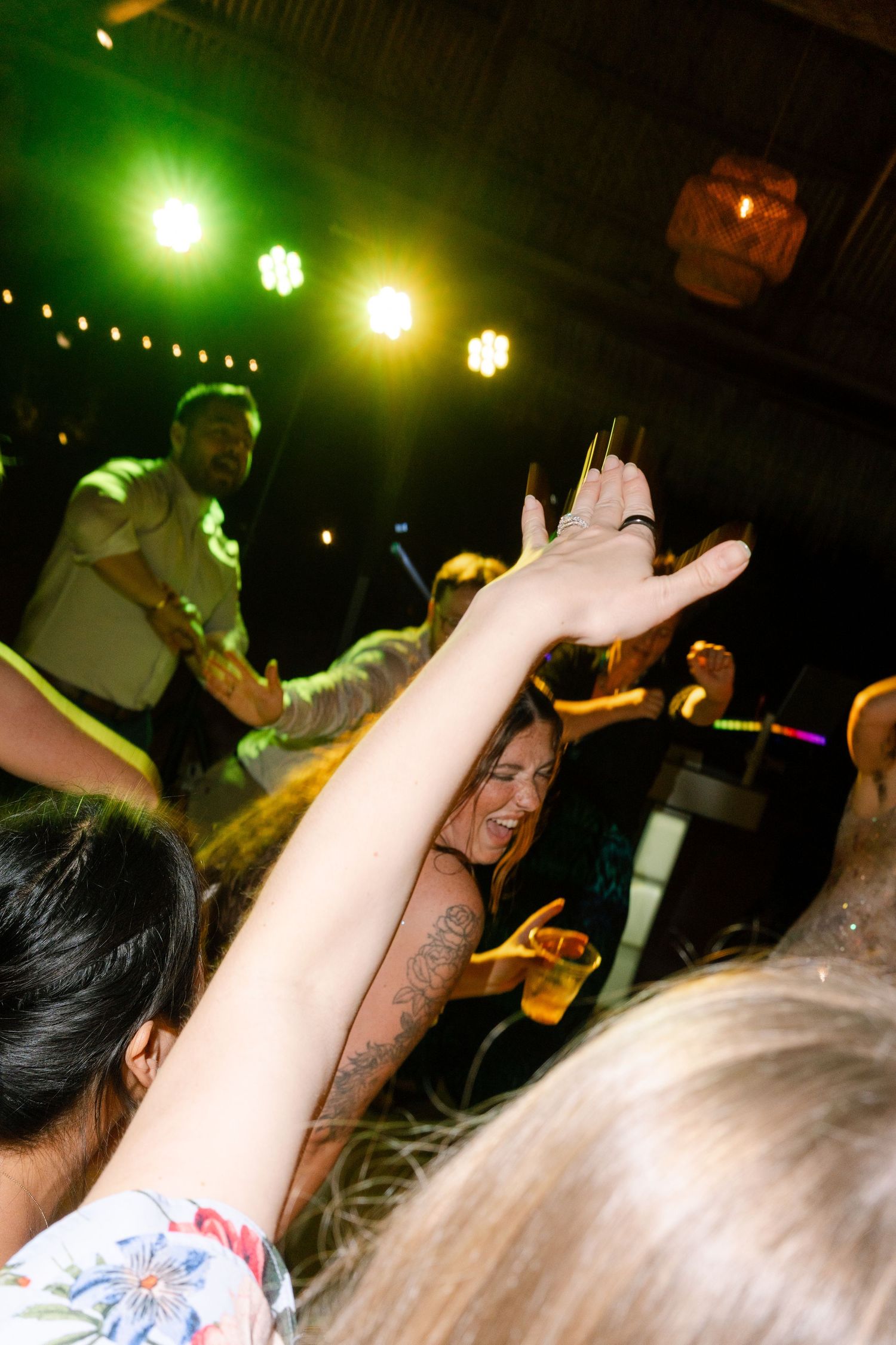 A crowd of people raising their hands at a live music event with colorful stage lights.