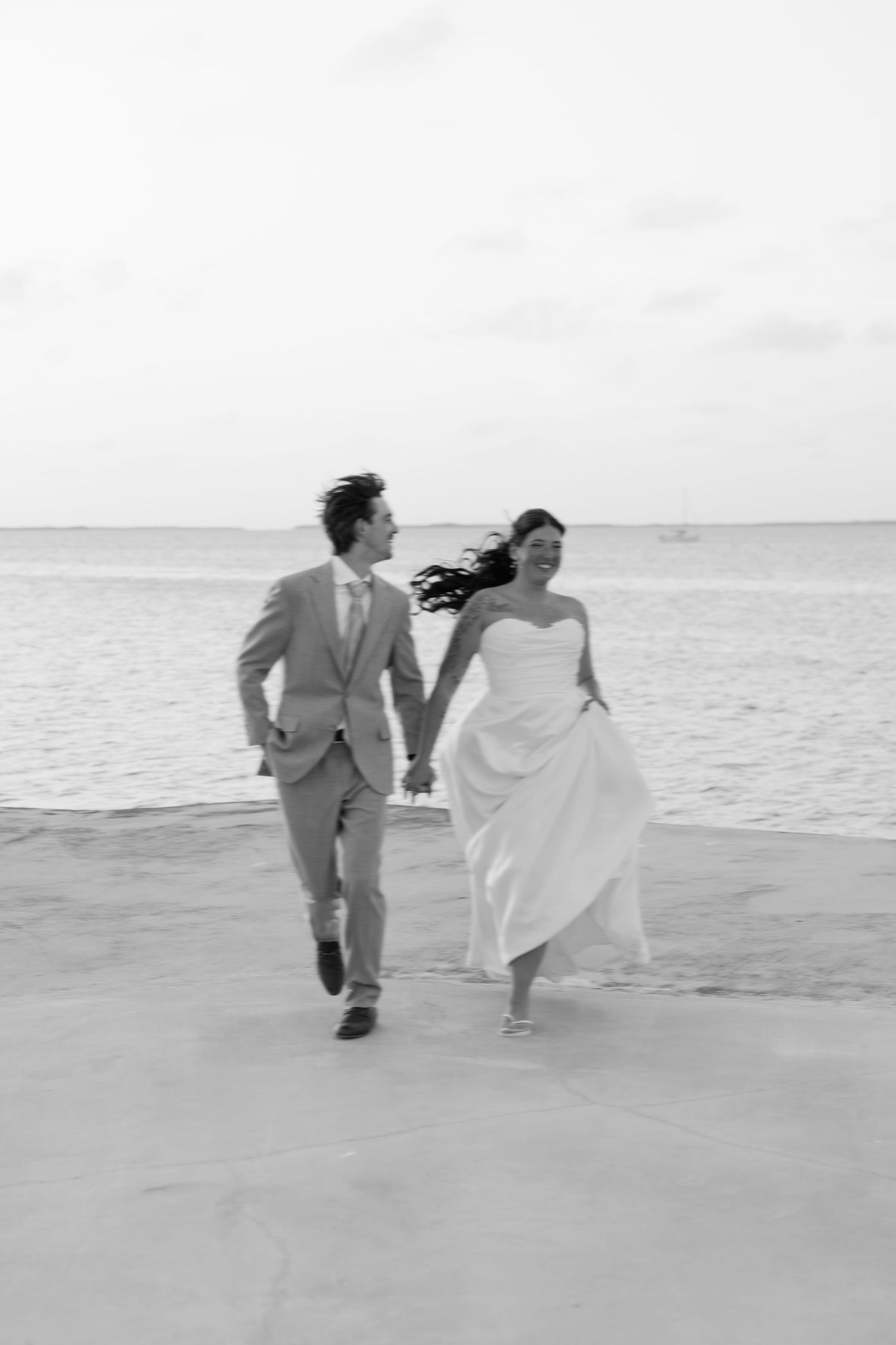 A bride and groom walking hand-in-hand on a beach.