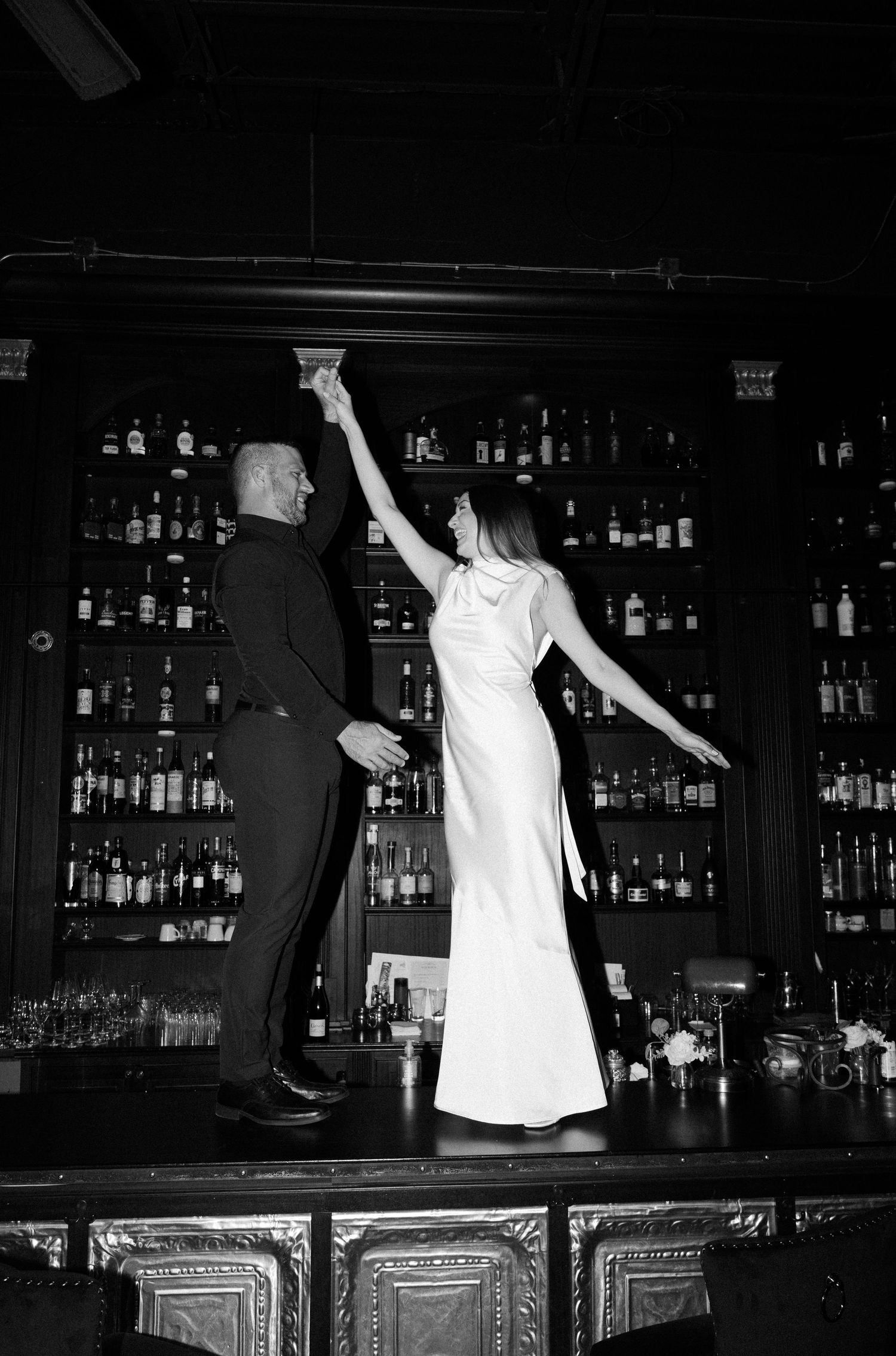 Black and white photo series shows a bartender dancing and flipping bottles in an energetic bar performance sequence.