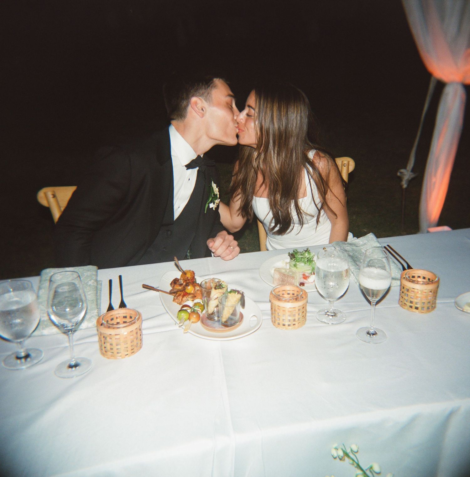 Bride and groom sharing a kiss at their wedding reception dinner table with elegant glassware and candles.