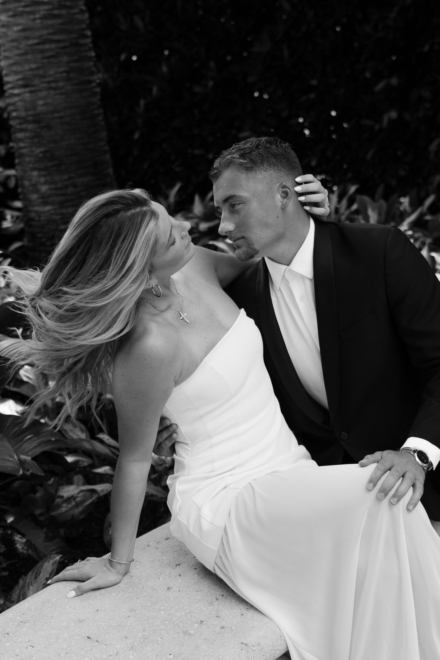 Black and white wedding photo of bride and groom sitting together outdoors, sharing a romantic moment.