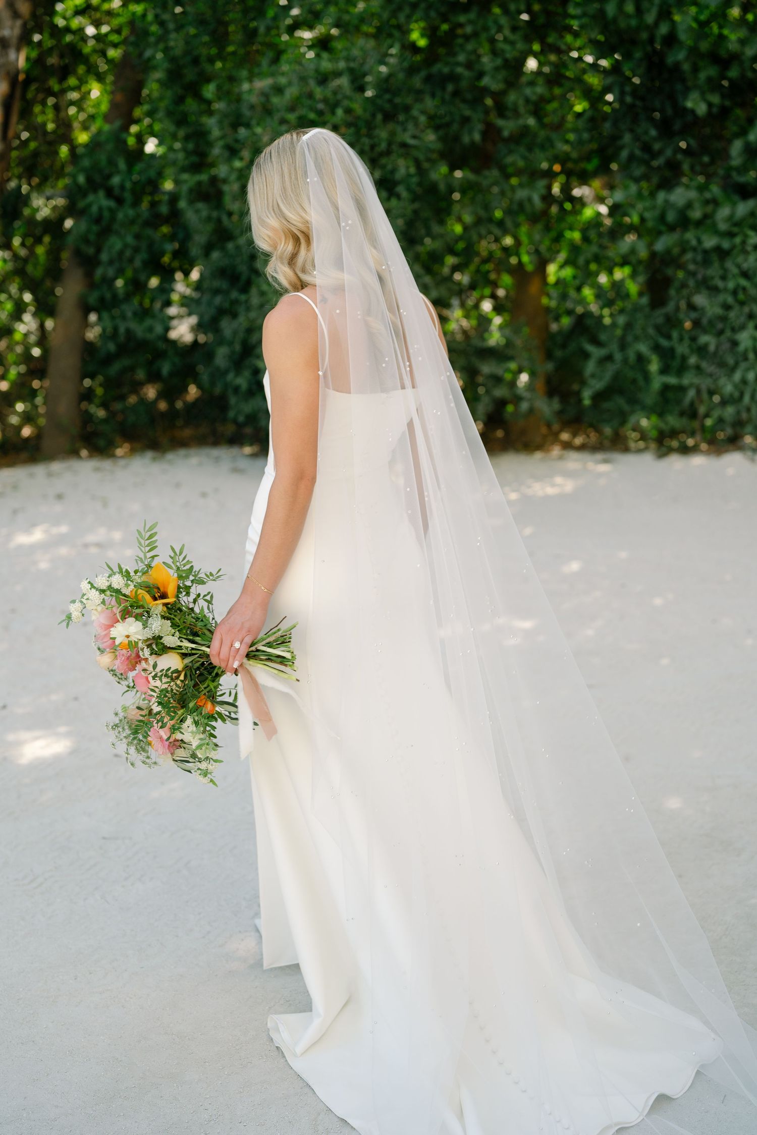 A flowing white wedding dress with a long veil captured in a series of elegant outdoor bridal portraits.