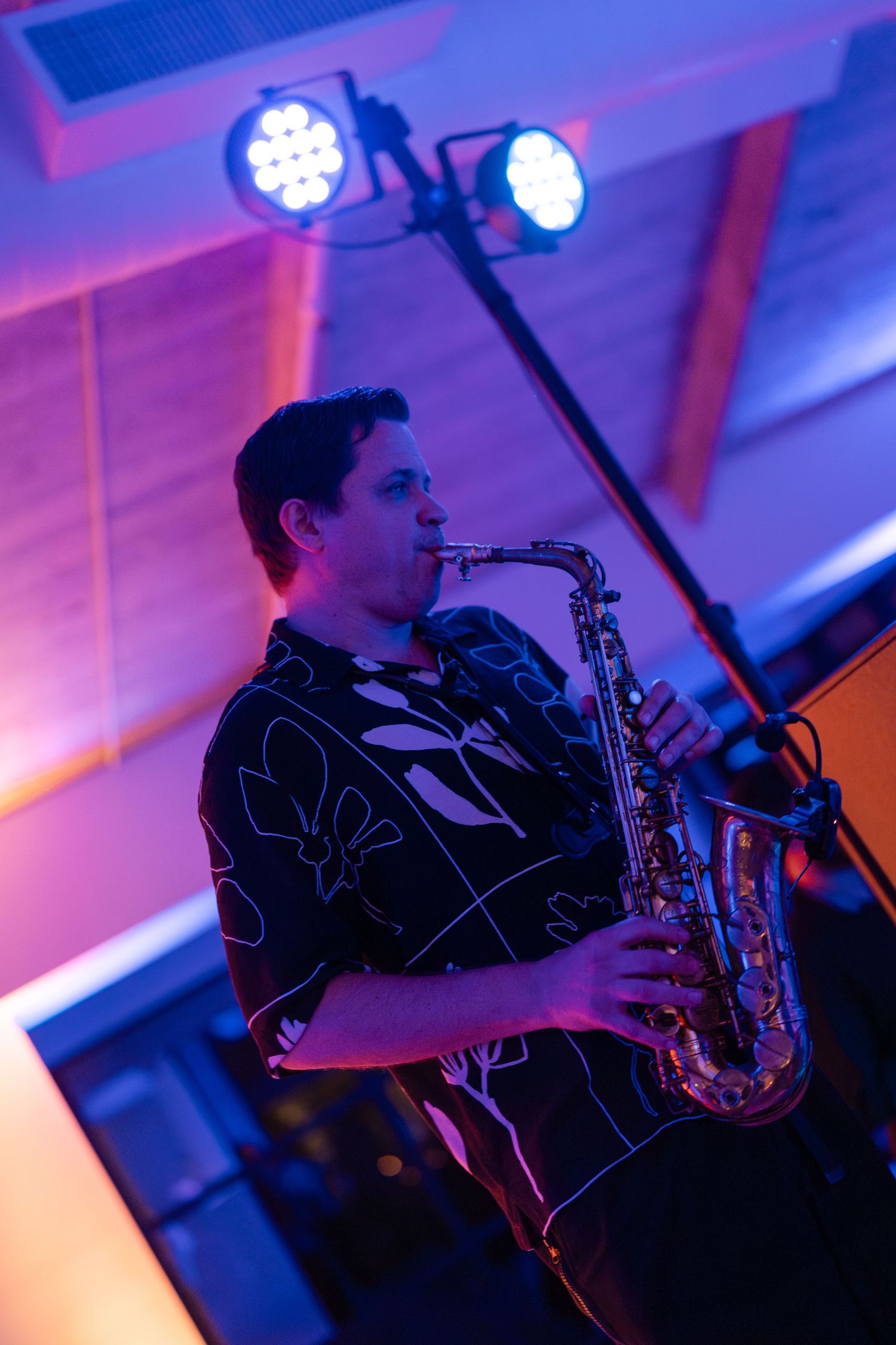 Saxophone player performing at event with dramatic purple and blue stage lighting.