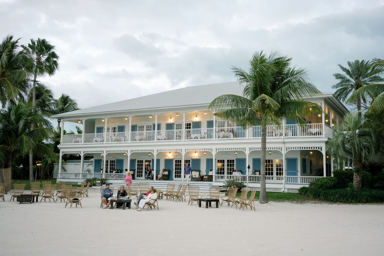 A panoramic view of a white beachfront resort with palm trees and lounge chairs along the shoreline.