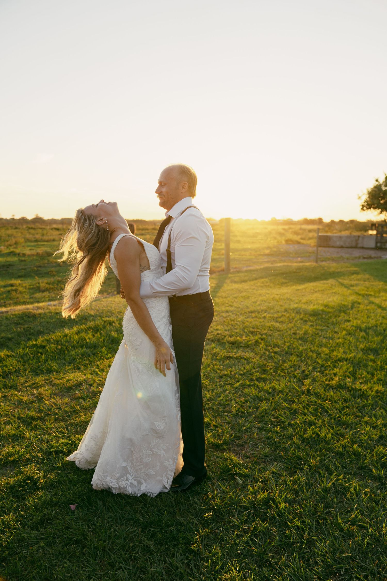 Couple embraces during sunset photo session in green meadow creating silhouettes and romantic shadows in golden light.