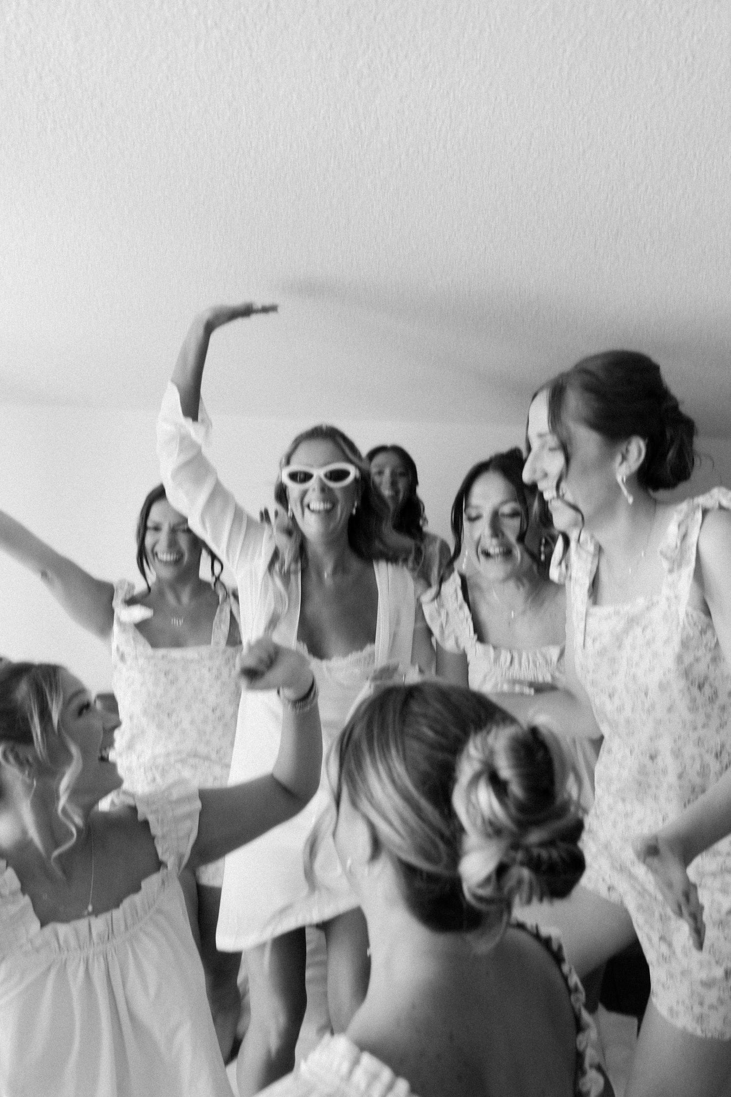 Bridesmaids in white dresses make silly faces and poses together during a fun pre-wedding photo session.