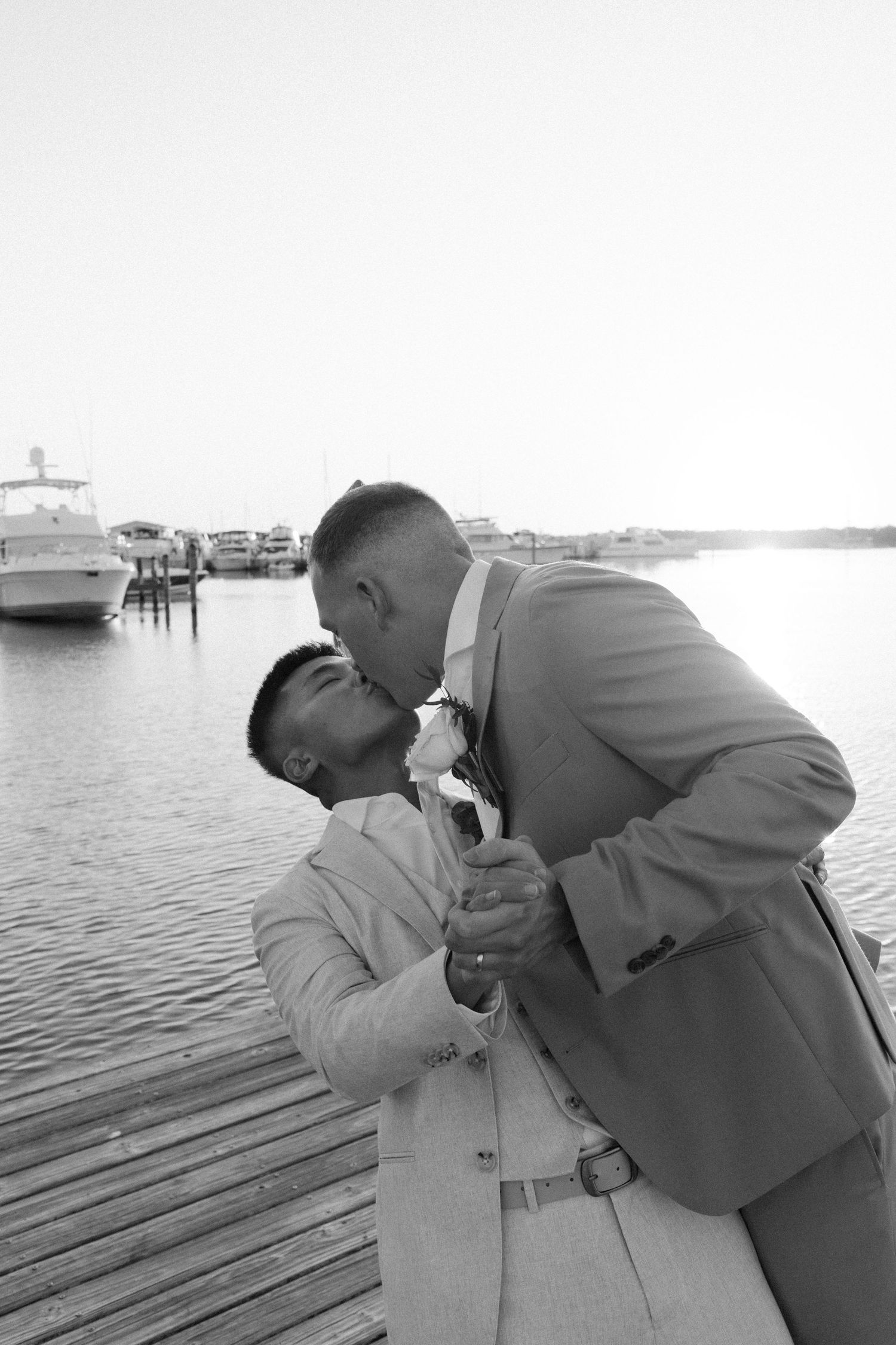 A romantic black and white moment shared between a couple on a wooden dock by the water.