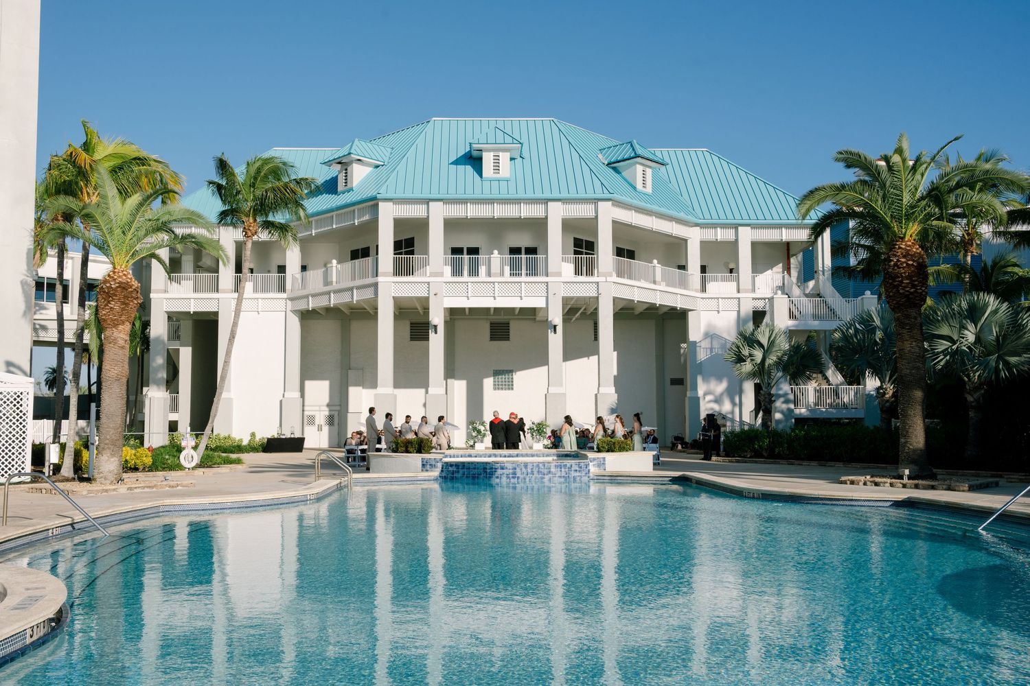 Panoramic view of a luxury resort pool area with white buildings and palm trees.