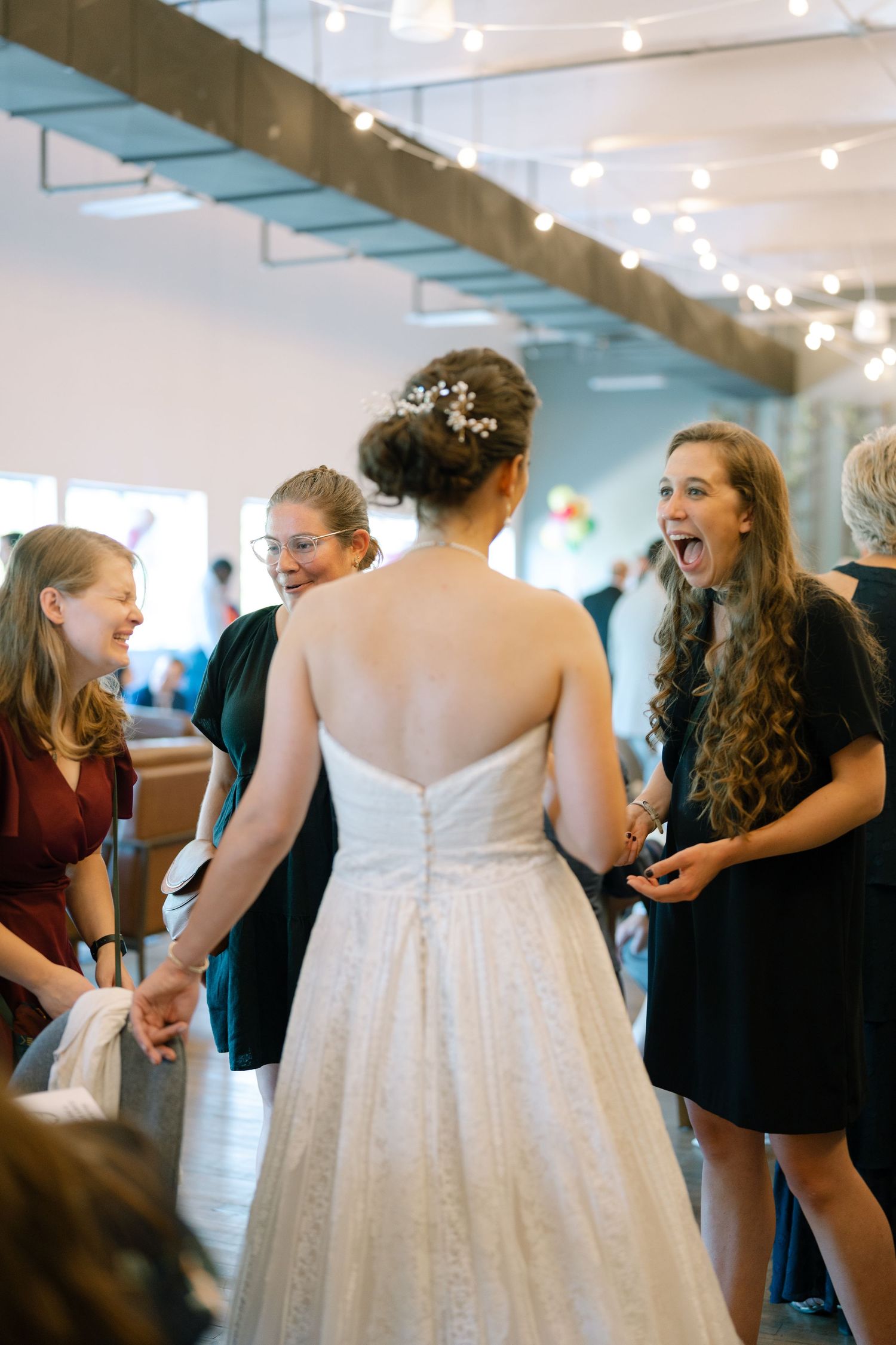Wedding celebration scene showing guests and bride in white dress interacting in bright indoor venue.