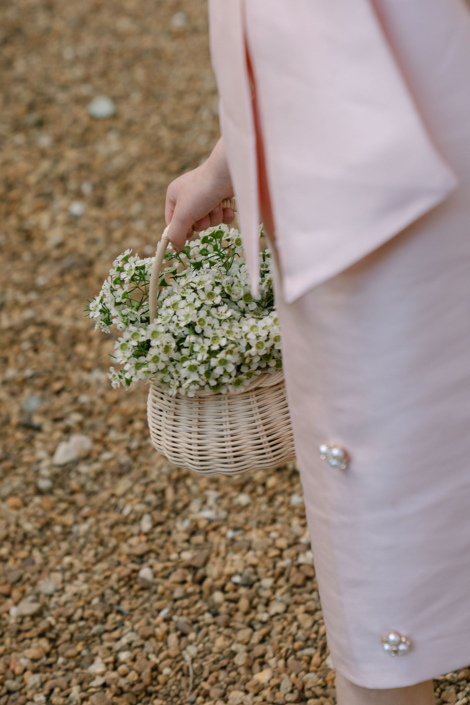Close-up of a woman in a pink dress holding a wicker basket filled with small white flowers.