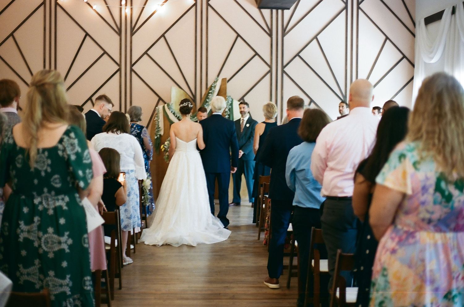Wedding ceremony taking place in an elegant chapel with art deco geometric ceiling details.