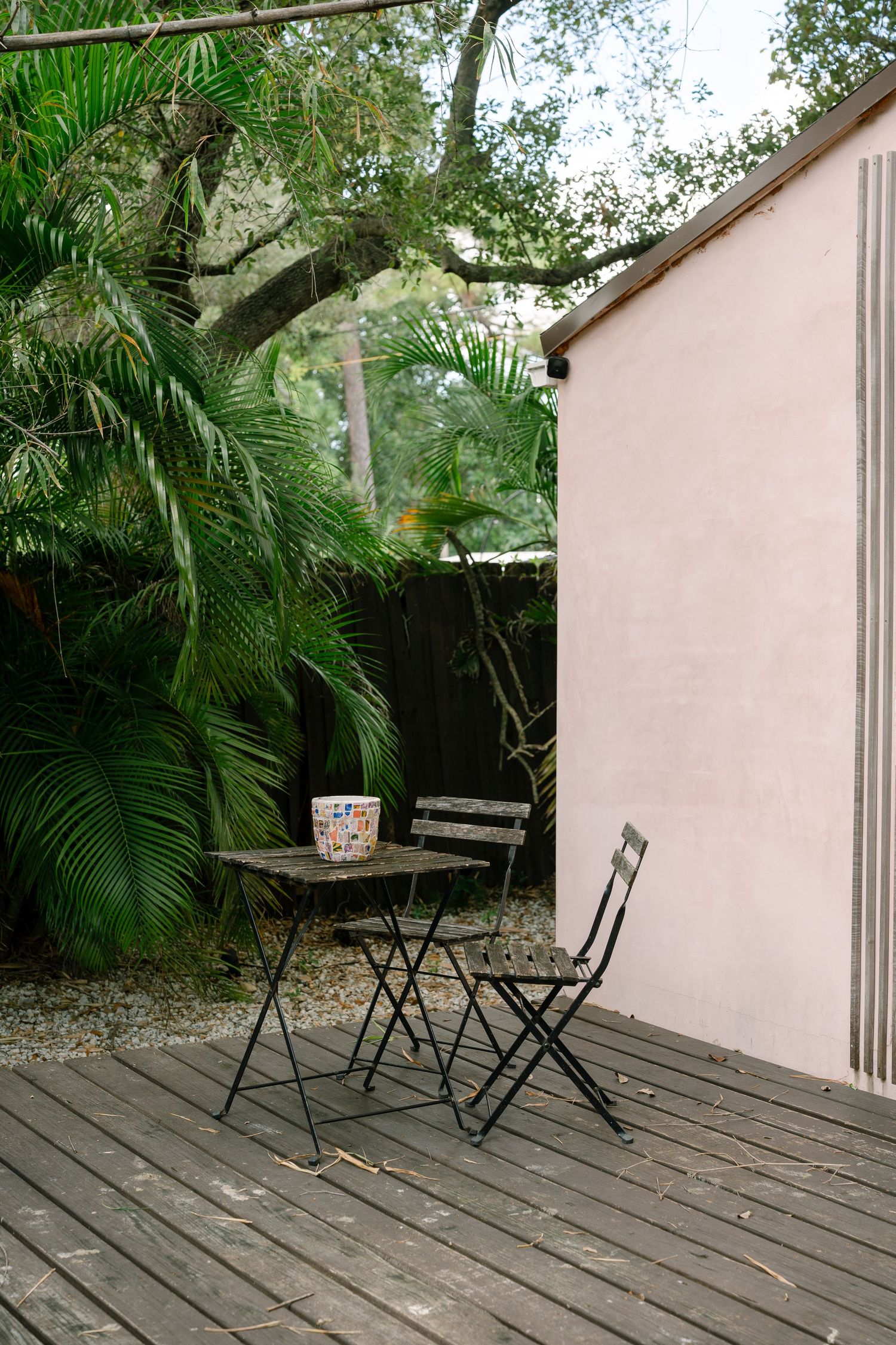 Peaceful outdoor seating area with folding chairs and palm trees against a pink wall.