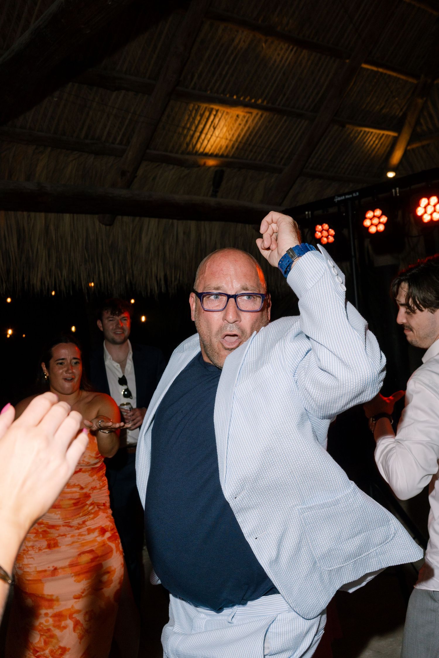 An older man in a white suit is dancing enthusiastically at what appears to be a party or celebration.