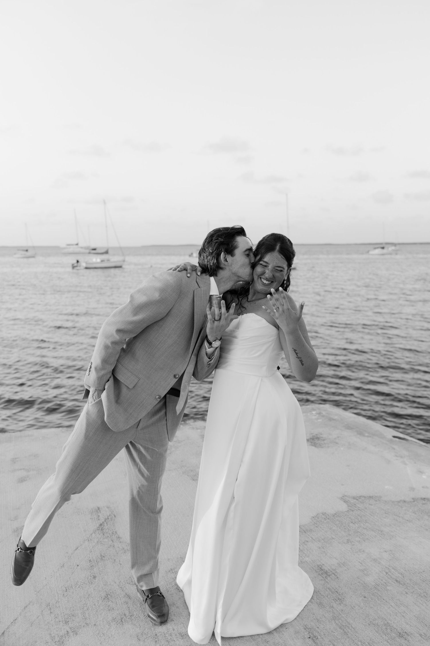A couple in wedding attire embracing on a beach with the ocean in the background.