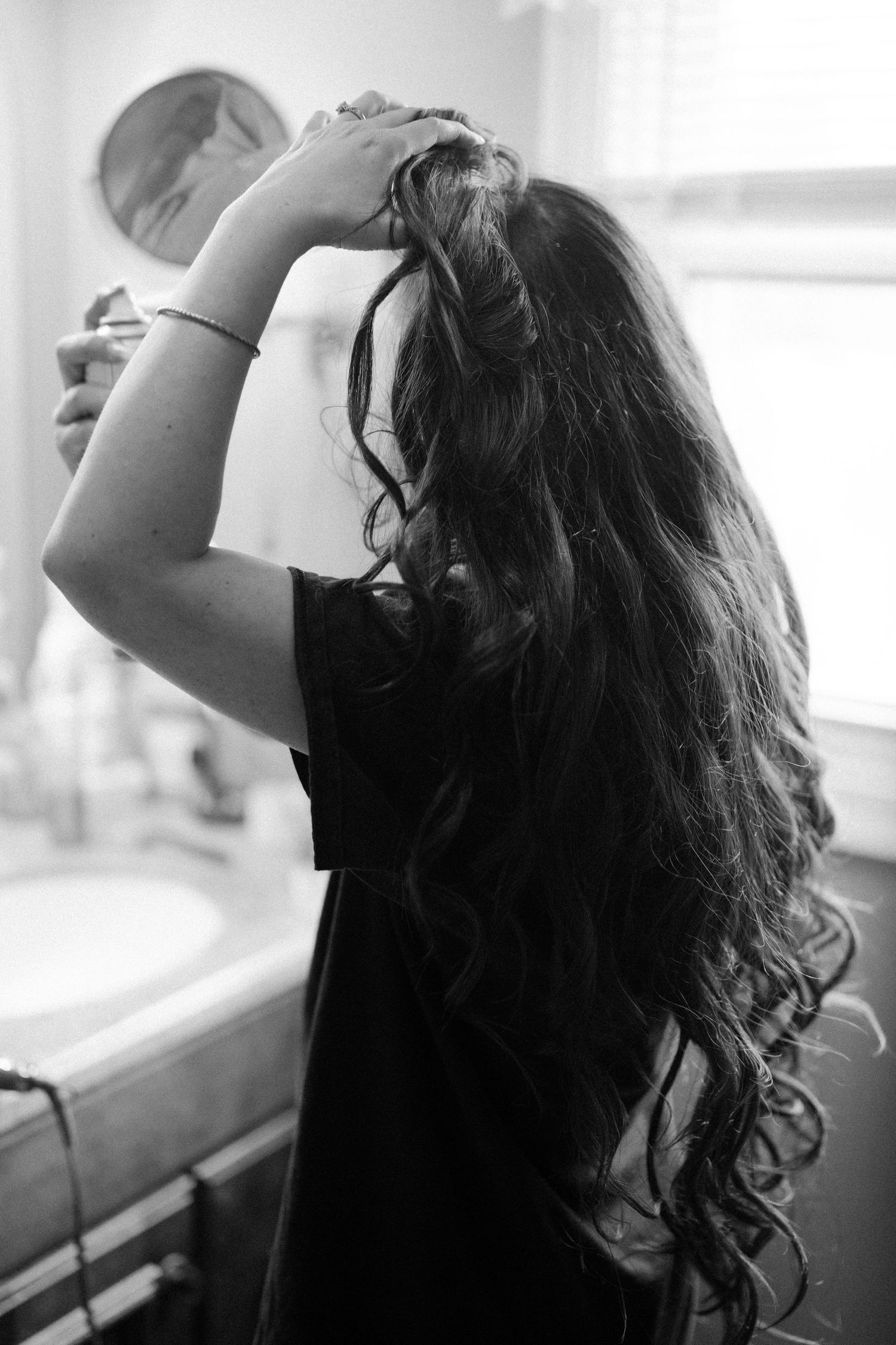 Silhouette of curly hair being styled against bright window light in black and white.
