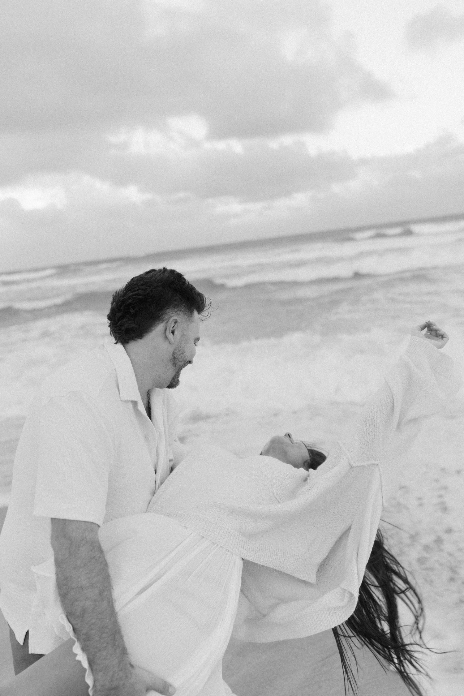 A romantic black and white photo sequence of a couple playing with a white sheet on a windy beach.