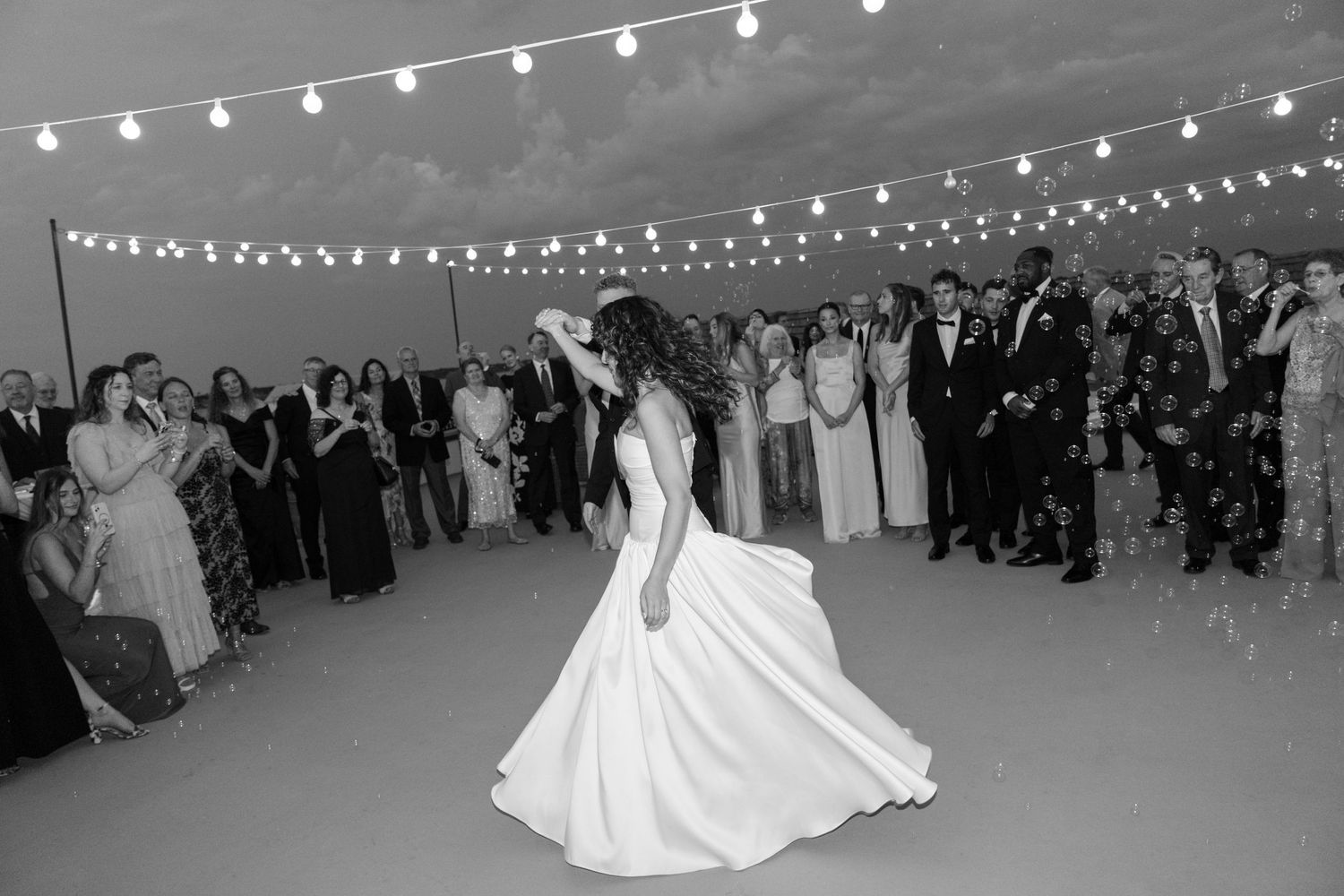 A wedding reception under string lights with the bride twirling in her white gown.
