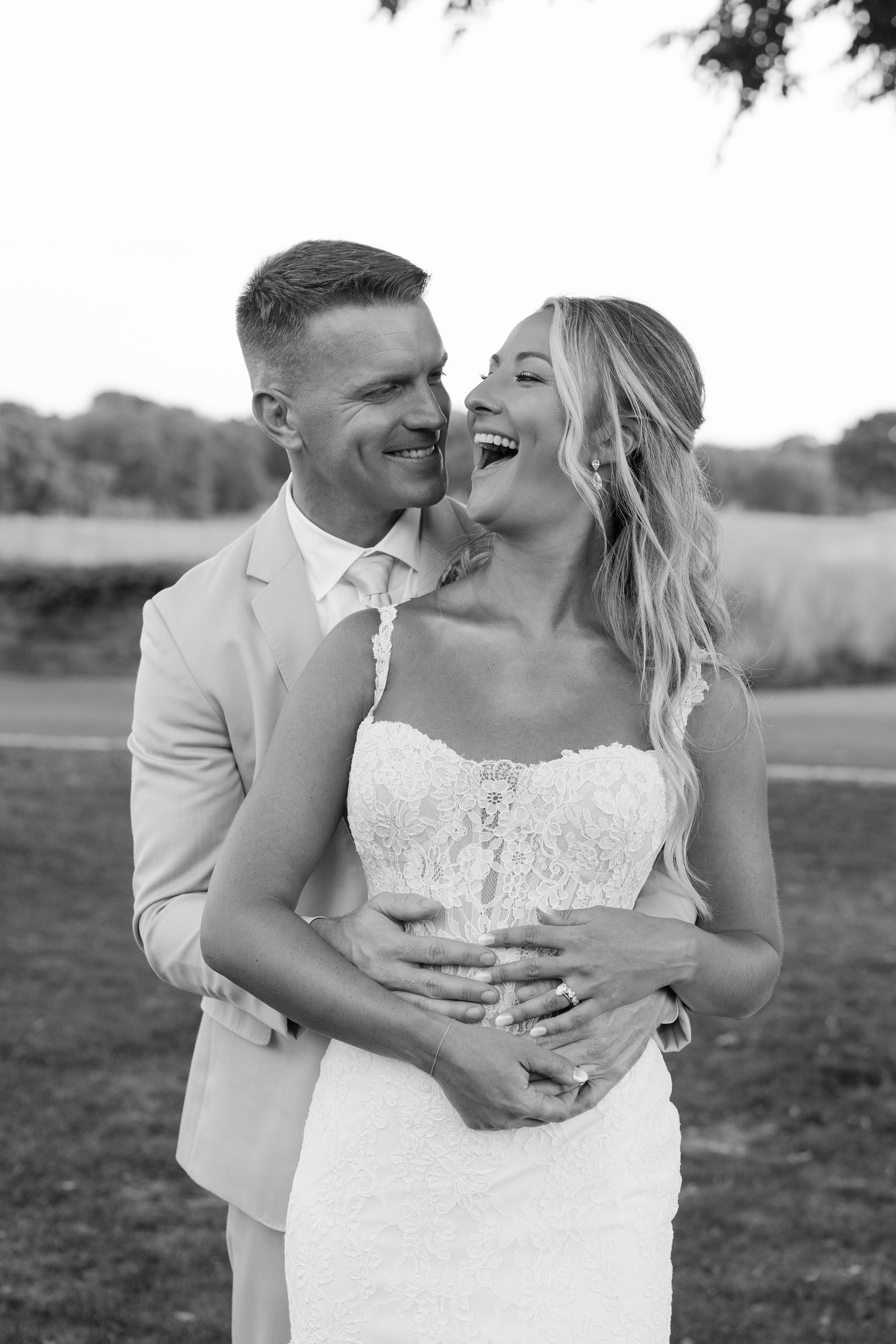 Black and white photo of a joyful bride and groom embracing outdoors on their wedding day.