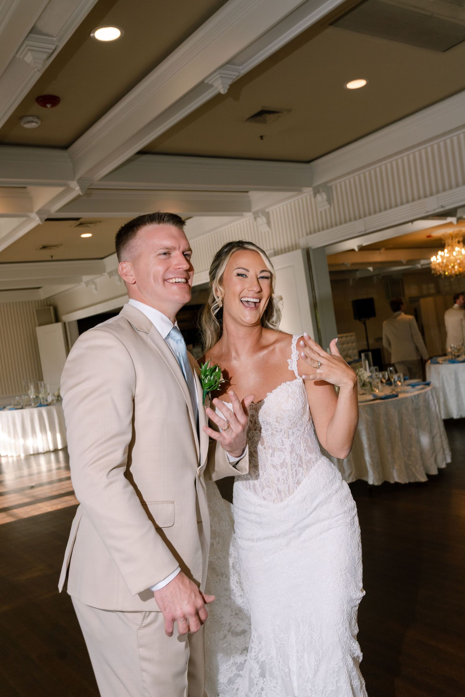 Joyful bride and groom laugh together during their wedding reception inside an elegant ballroom venue.