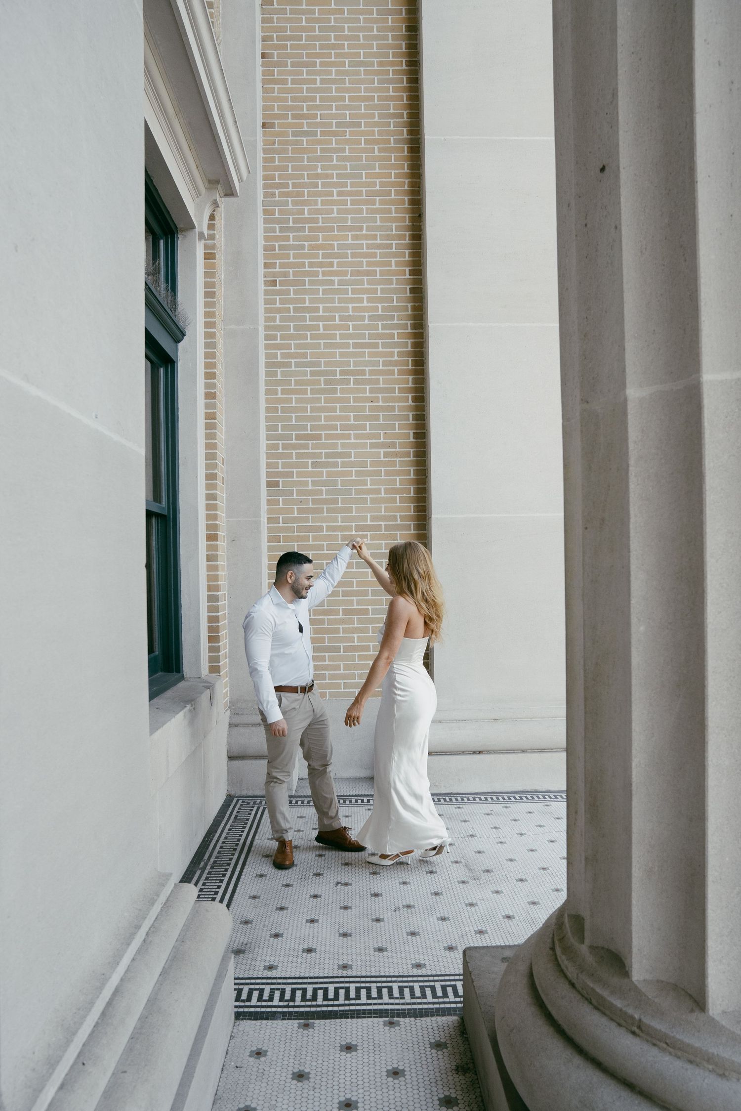 A romantic couple in wedding attire sharing intimate moments under elegant white columns on a tiled porch.