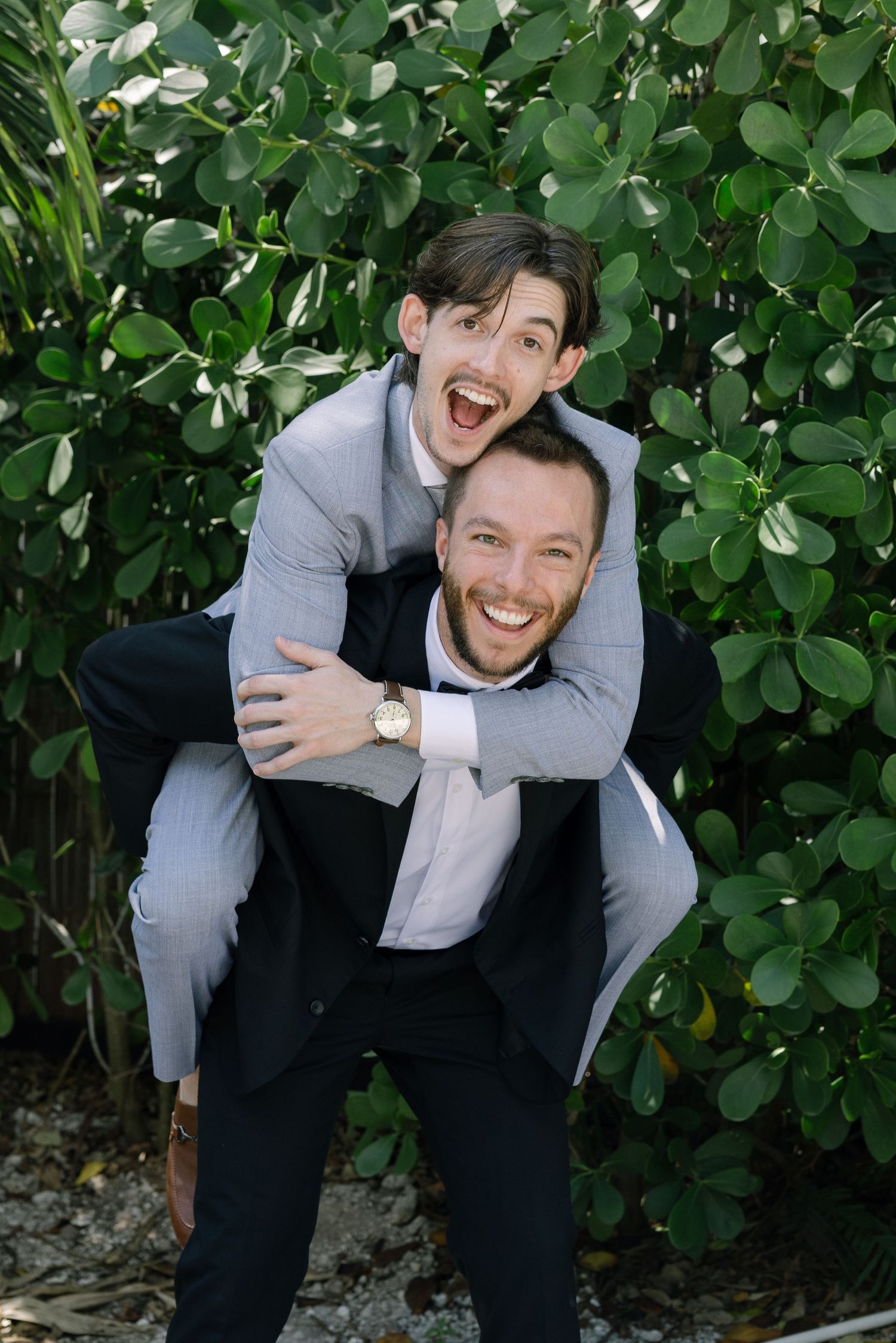A man and a woman embrace and laugh joyfully in a lush, green setting.