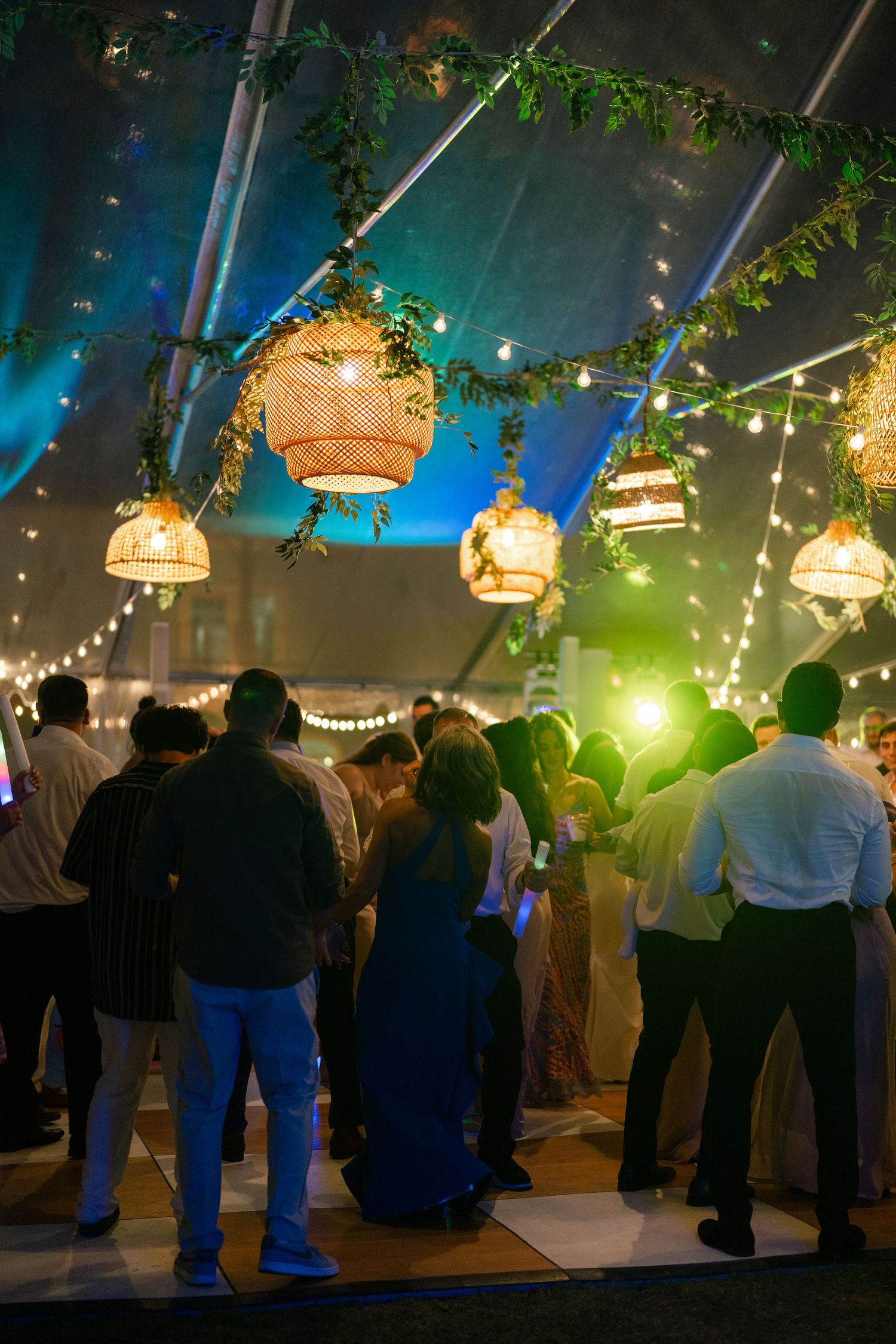 Wedding guests dance under wicker pendant lights and string lights inside a beautifully decorated evening tent.
