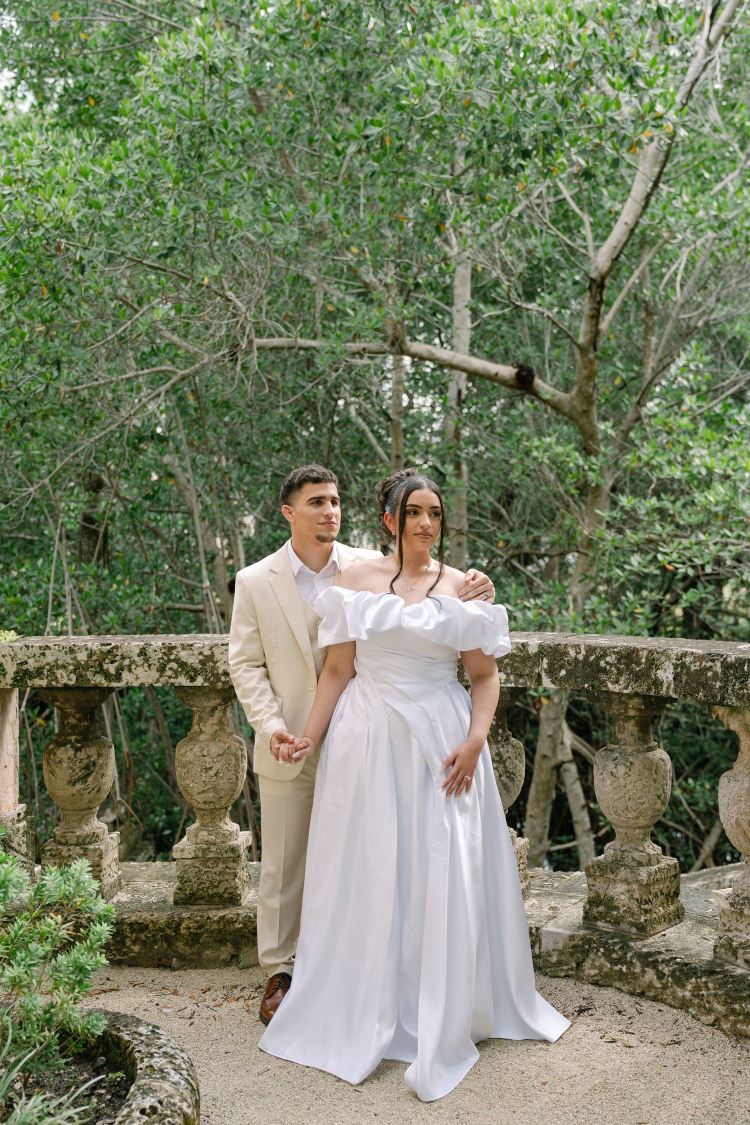 A family wearing white clothing poses for a photo series in a lush garden path with decorative stone elements.