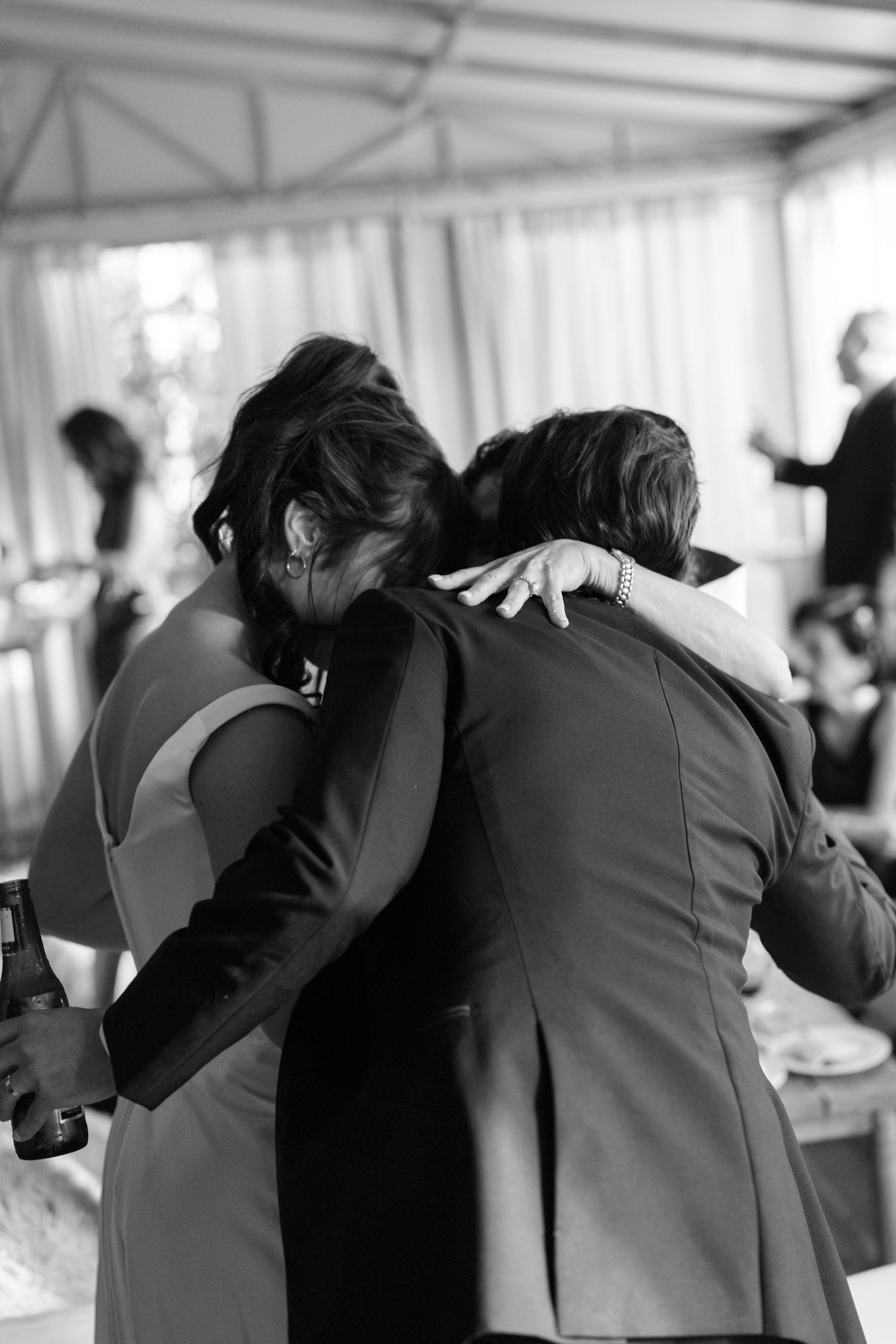 Wedding party members in formal attire hugging in a group during celebration.