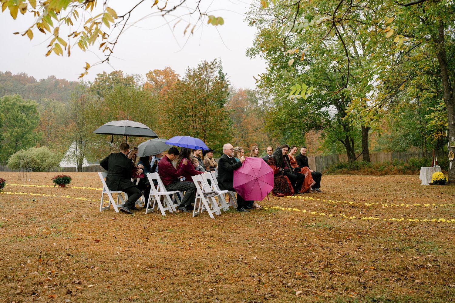Guests gather on a plowed field with umbrellas during an outdoor autumn event.