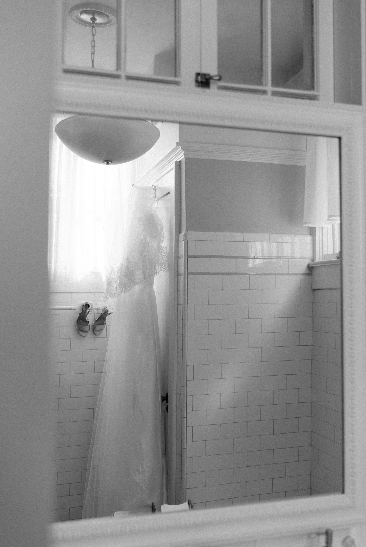 A black and white photograph shows a bathroom interior with white subway tile walls and a large mirror mounted above.